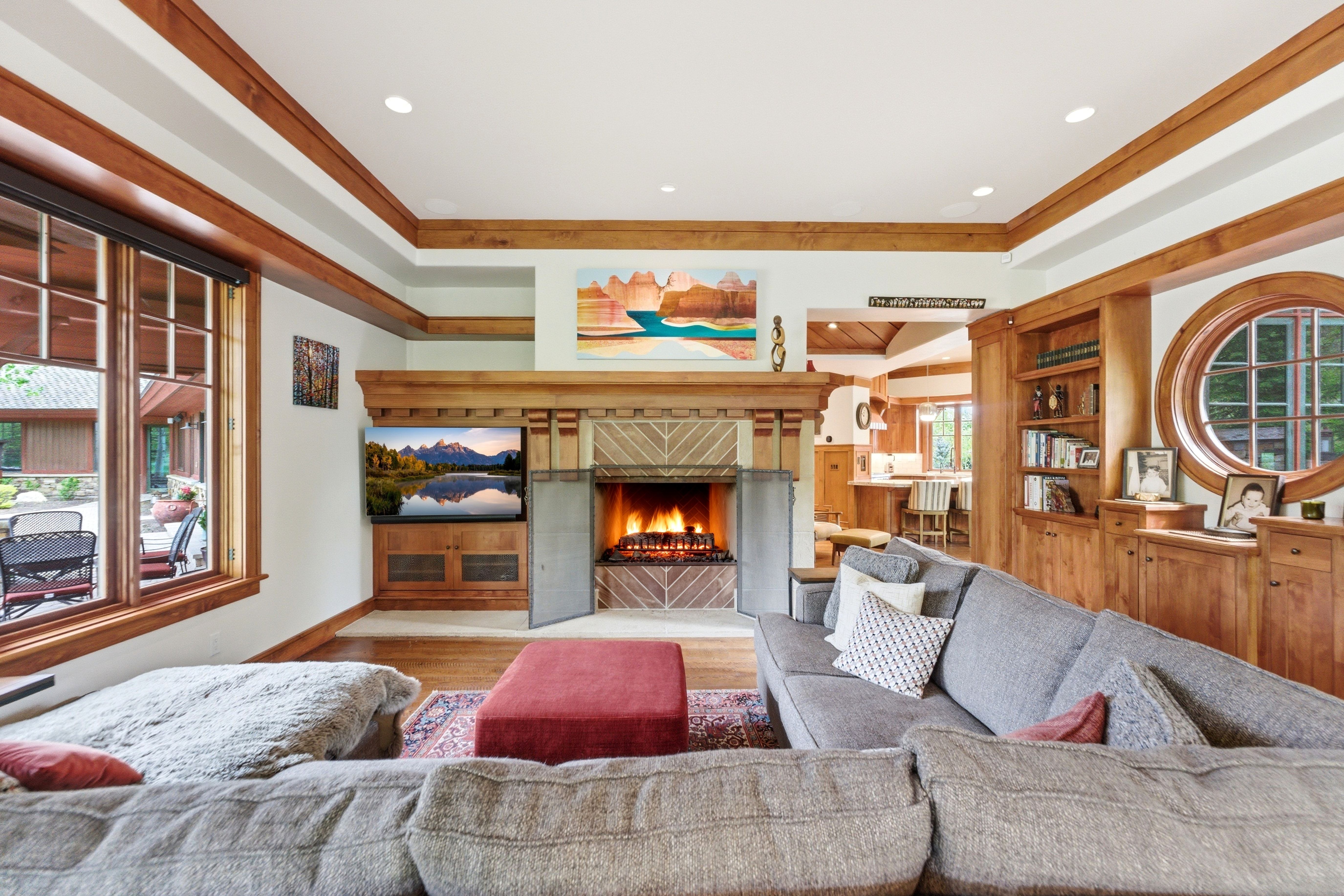 Living area featuring a stone fireplace with a wood mantel, wood-finish flooring, built-in wooden cabinetry, a circular window, and large picture windows