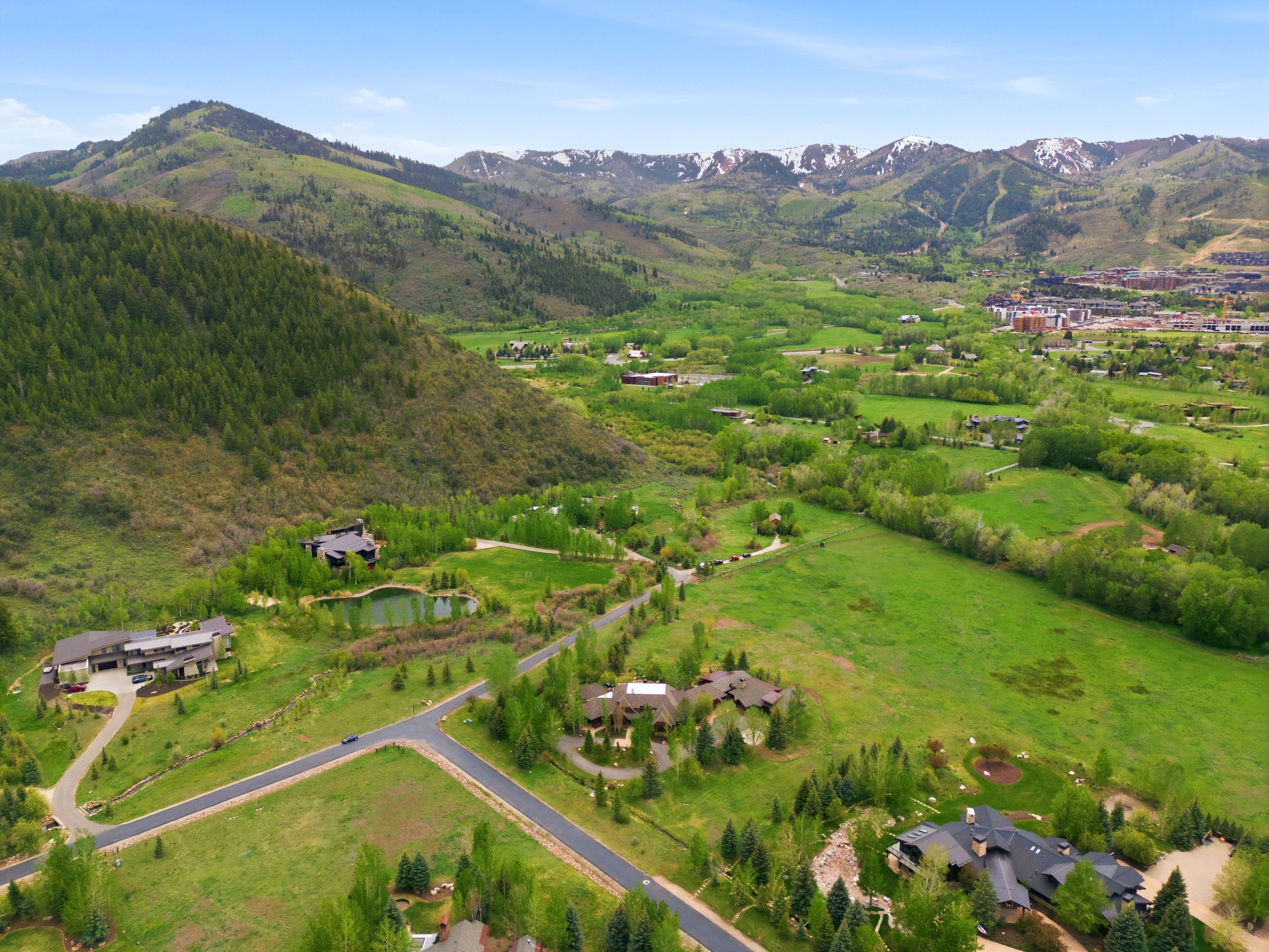 Expansive mountain landscape featuring varied topography, lush green fields, scattered residential structures, and distant snow-capped peaks