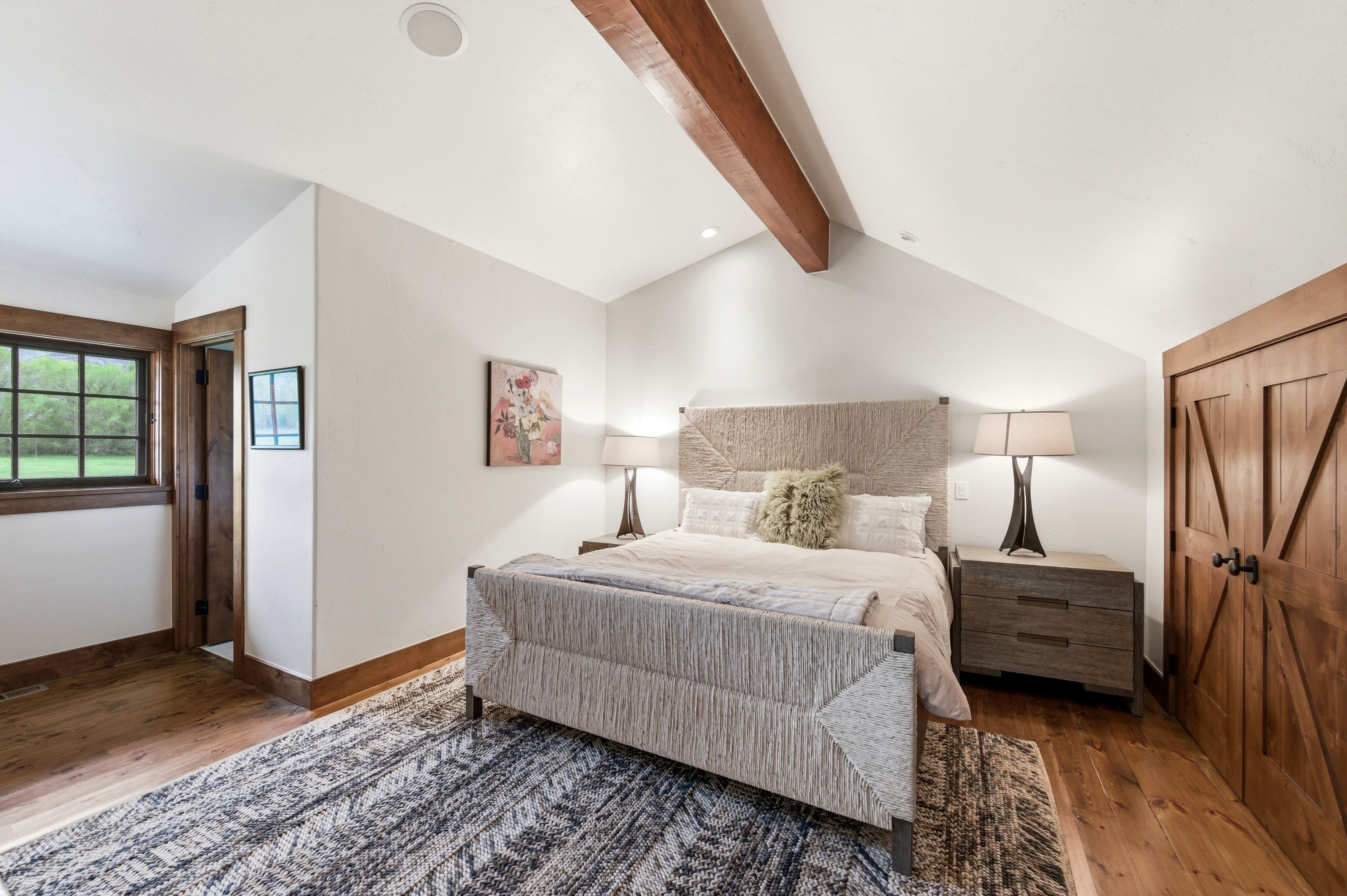 Spacious room featuring wood-finish flooring, a vaulted ceiling with exposed wood beams, and a window with dark trim