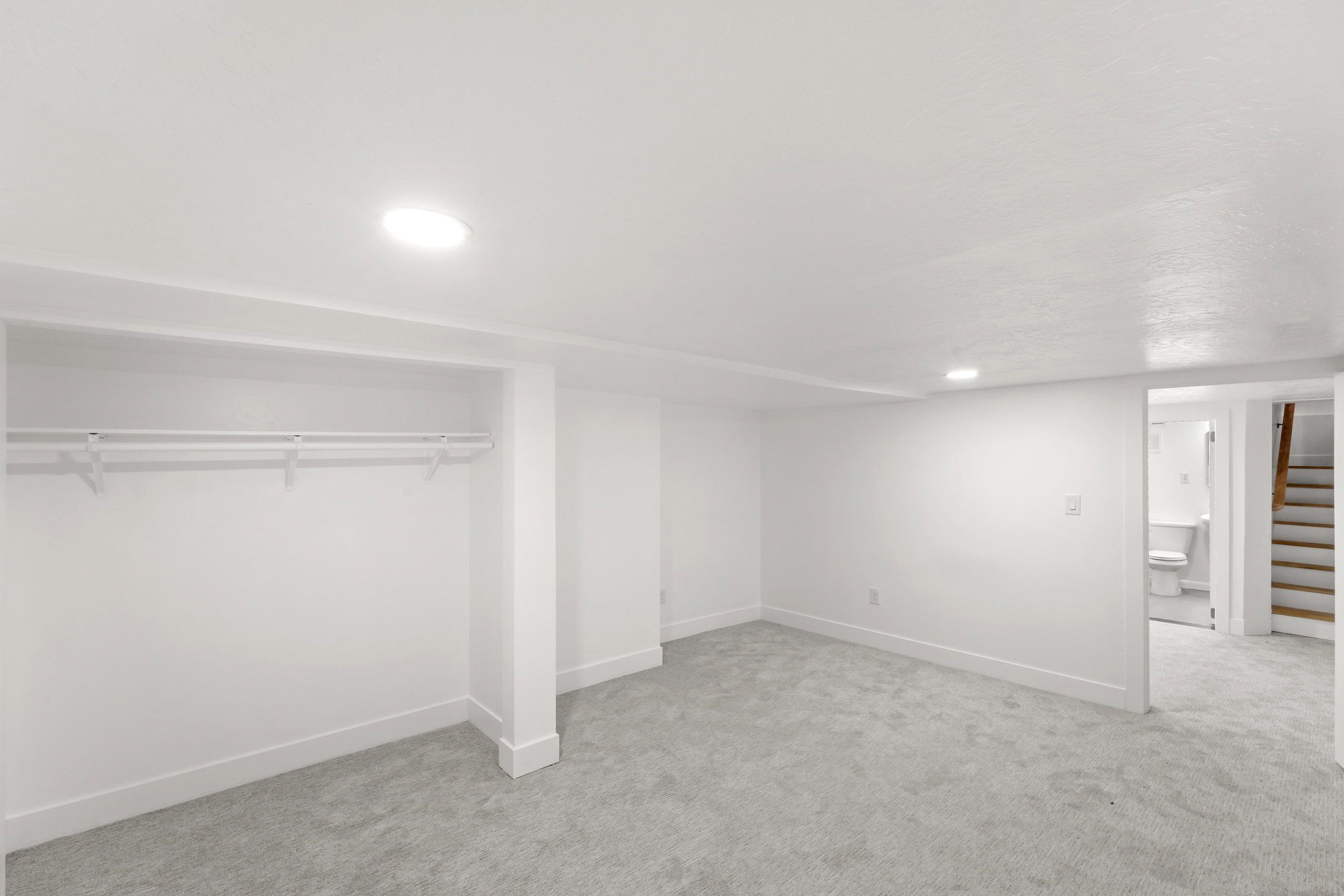 Spacious room with new gray carpeting, crisp white walls, and recessed lighting
