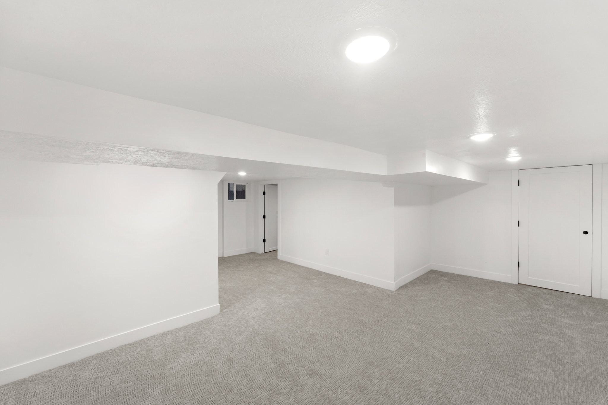 Spacious room featuring light gray carpeting, white painted walls, recessed lighting, and white baseboards