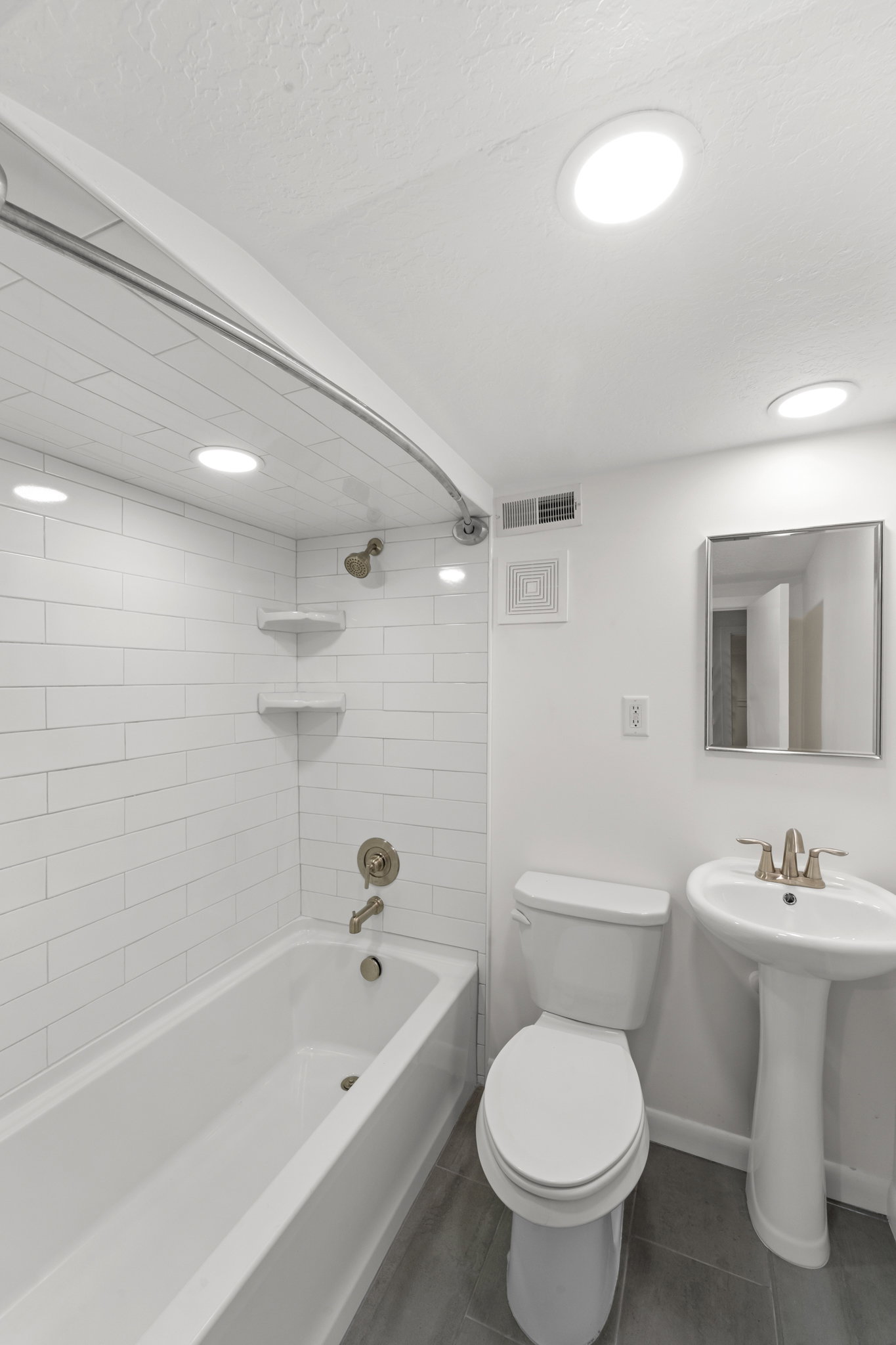 Bathroom featuring a white bathtub with subway tile surround, pedestal sink, toilet, and gray tile flooring