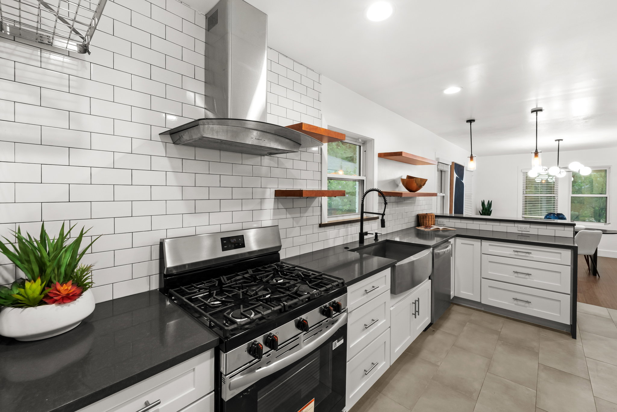 Modern kitchen featuring white shaker cabinetry, dark countertops, a stainless steel range with matching hood, and a farmhouse sink with a gooseneck faucet