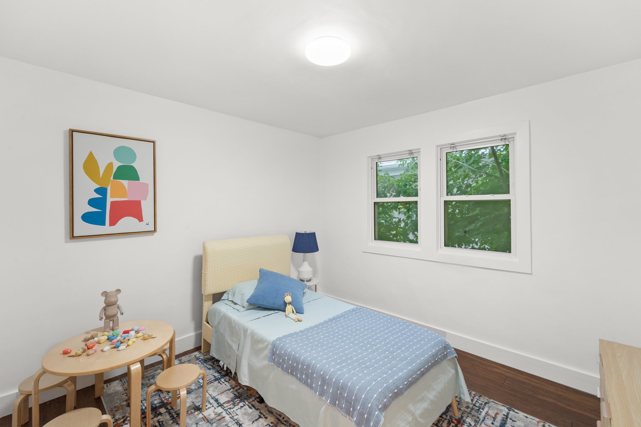 Bedroom featuring wood-finish flooring, two large windows, white trim, and a flush-mount ceiling light