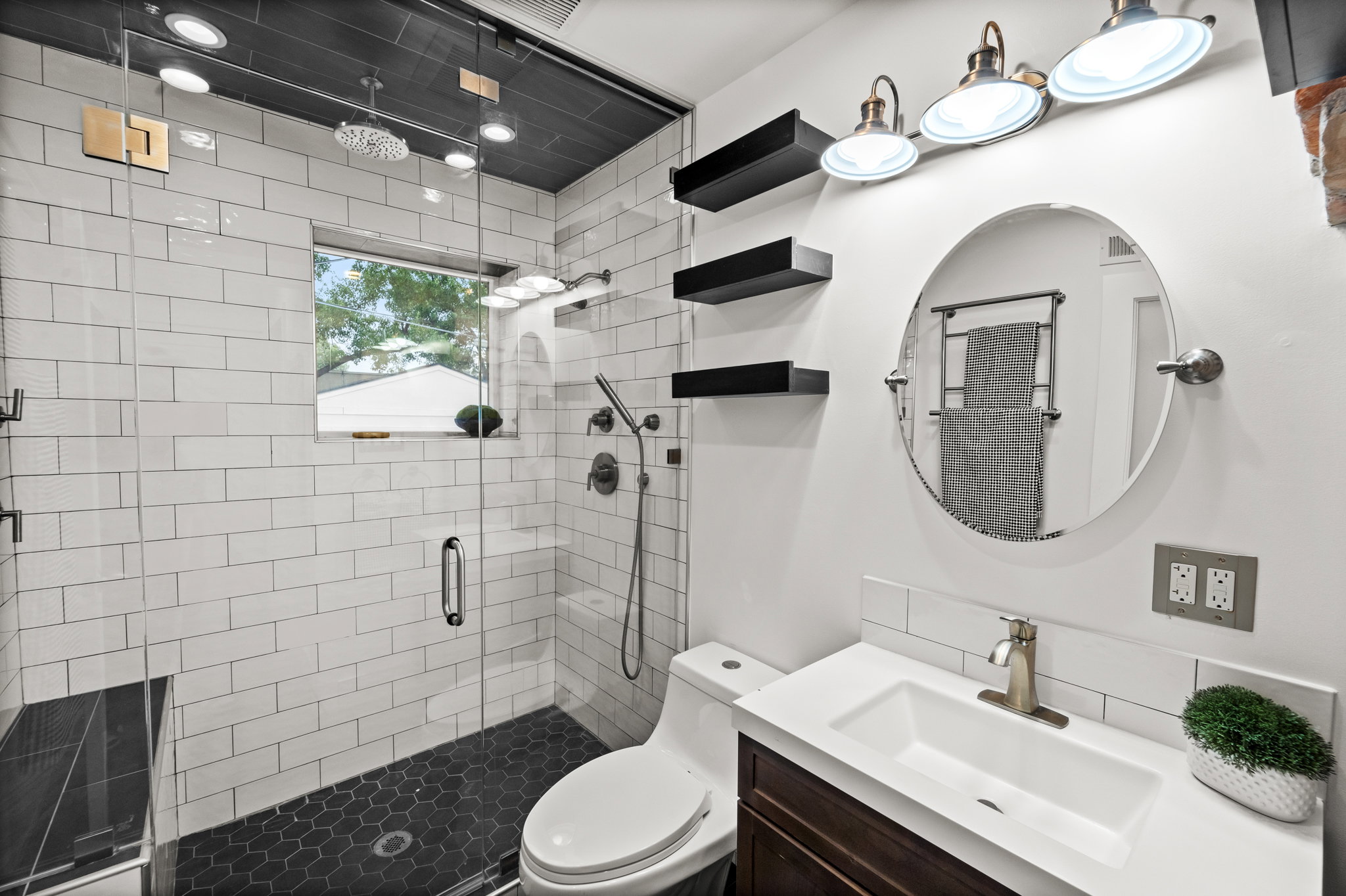 Contemporary bathroom featuring a spacious glass-enclosed shower with white subway tile walls and dark hexagonal floor tile