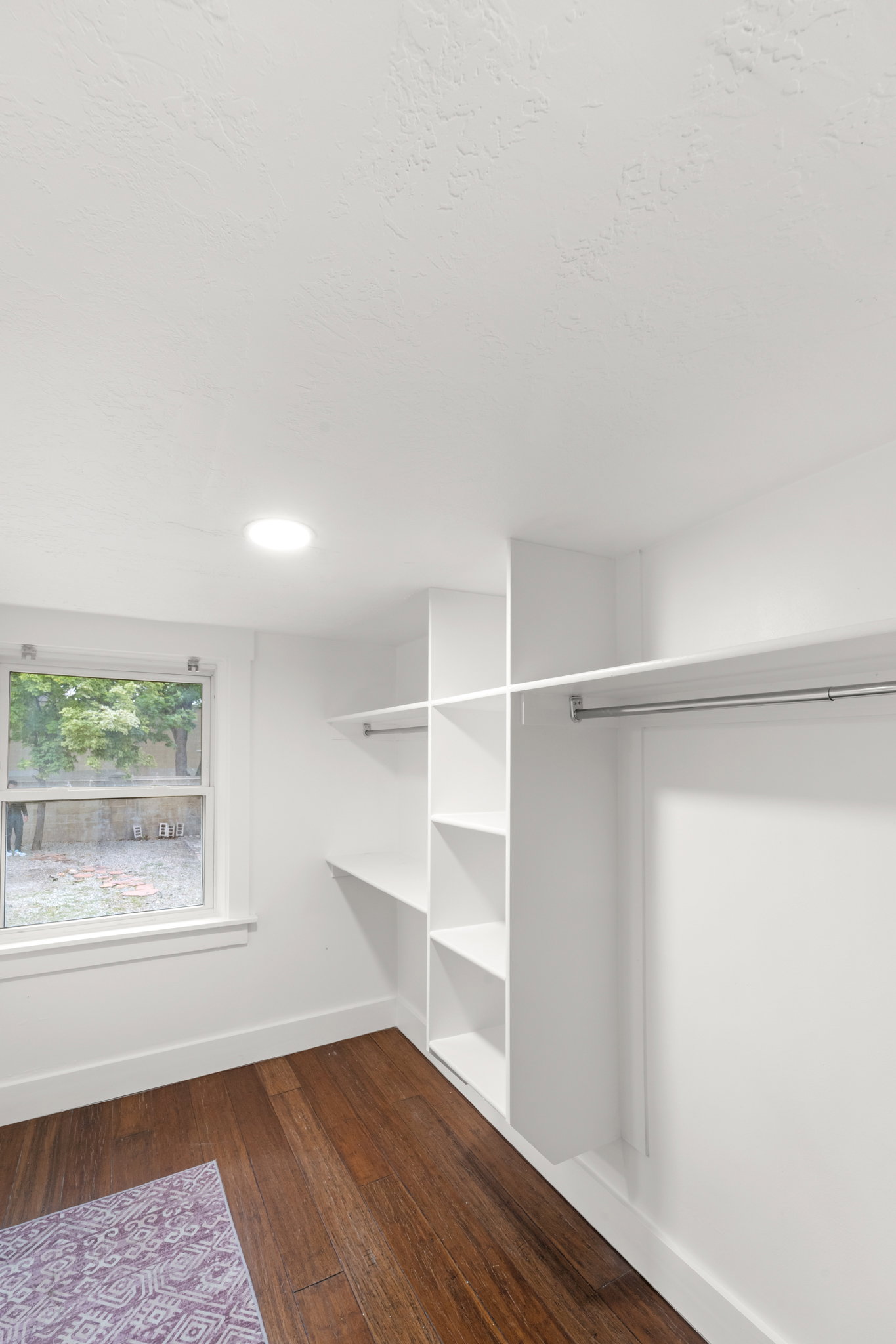 Primary bedroom walk-in closet with built-in shelving, hanging rods, recessed lighting, wood-finish flooring, and a window providing natural light