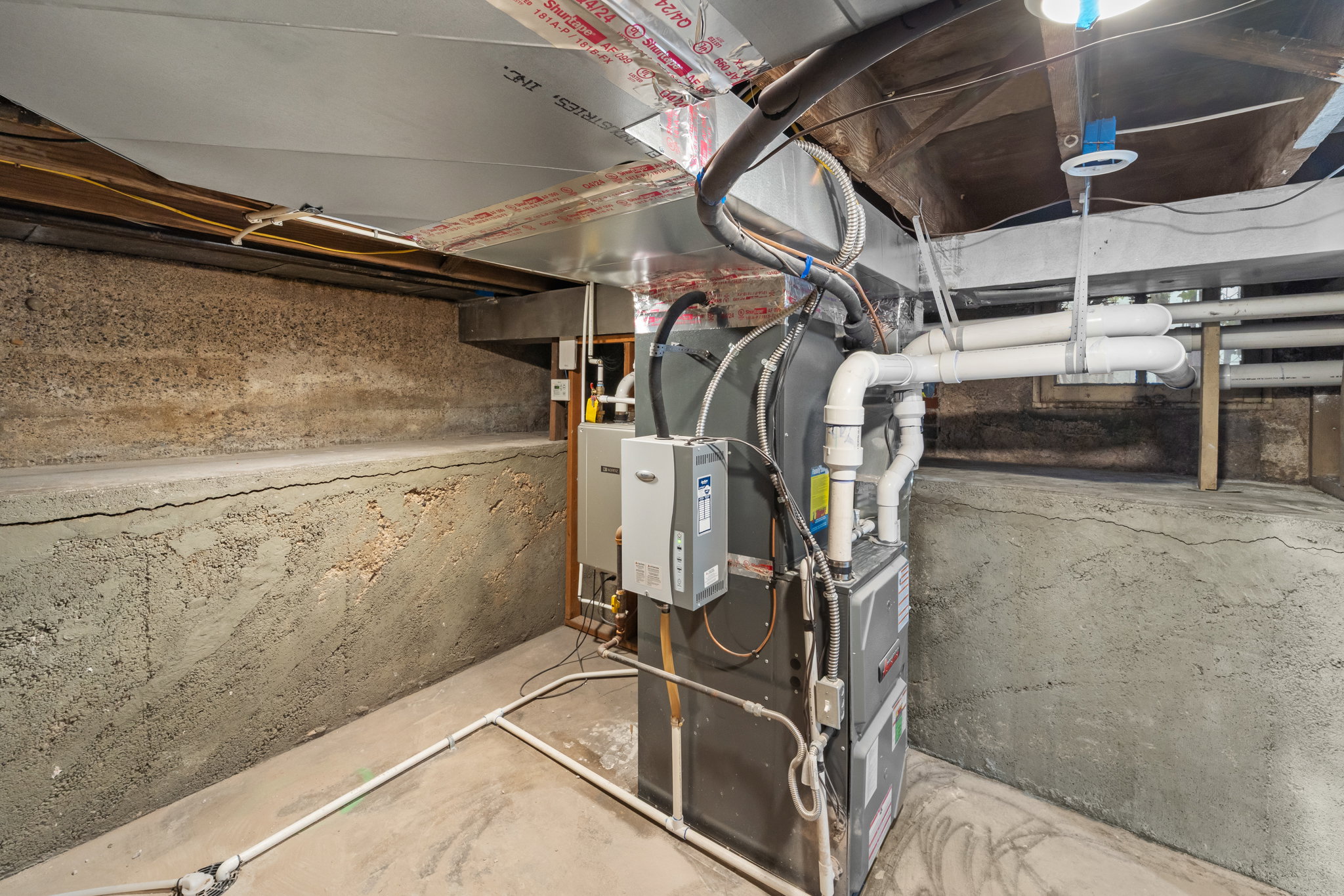 Utility area featuring a furnace system and water heater, exposed concrete walls, and overhead ductwork
