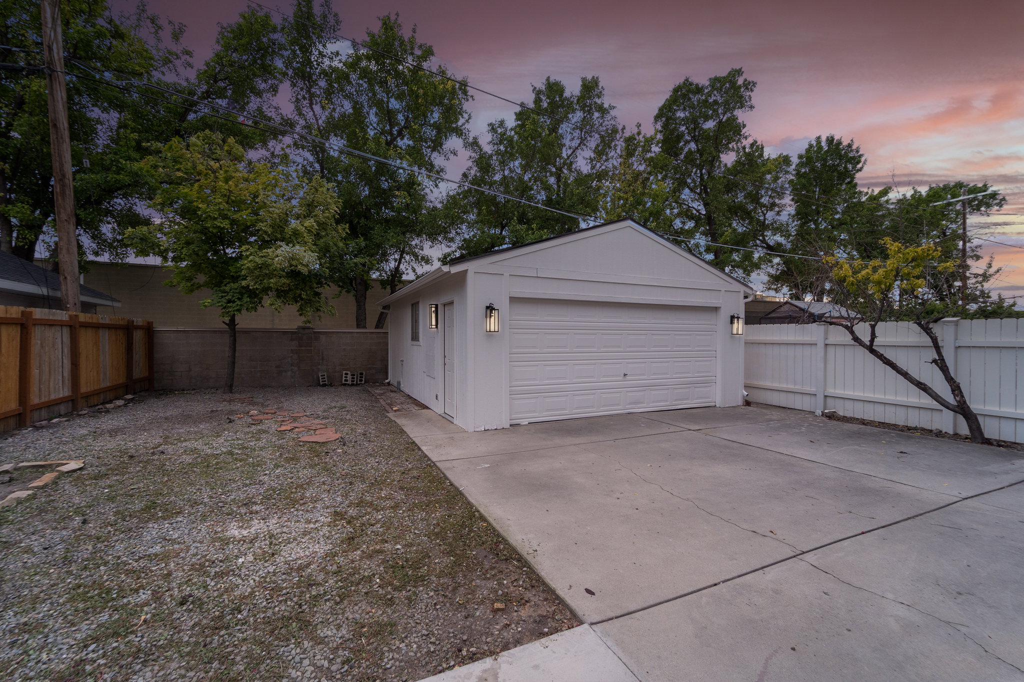 Detached white garage featuring a two-car garage door, two exterior wall sconces, and a side entrance