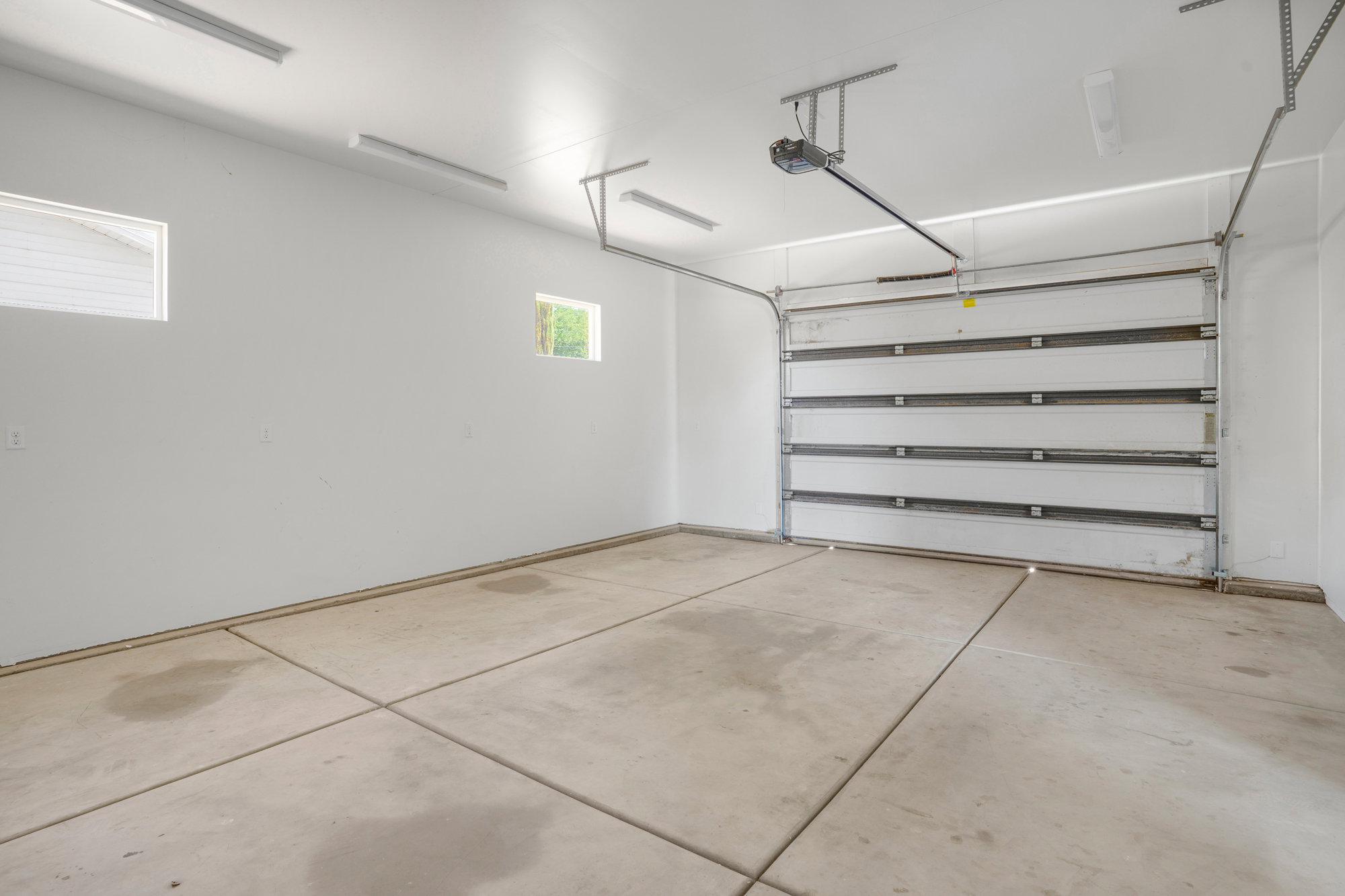 Spacious garage featuring a concrete floor, overhead lighting, two wall-mounted windows, and an automated sectional garage door