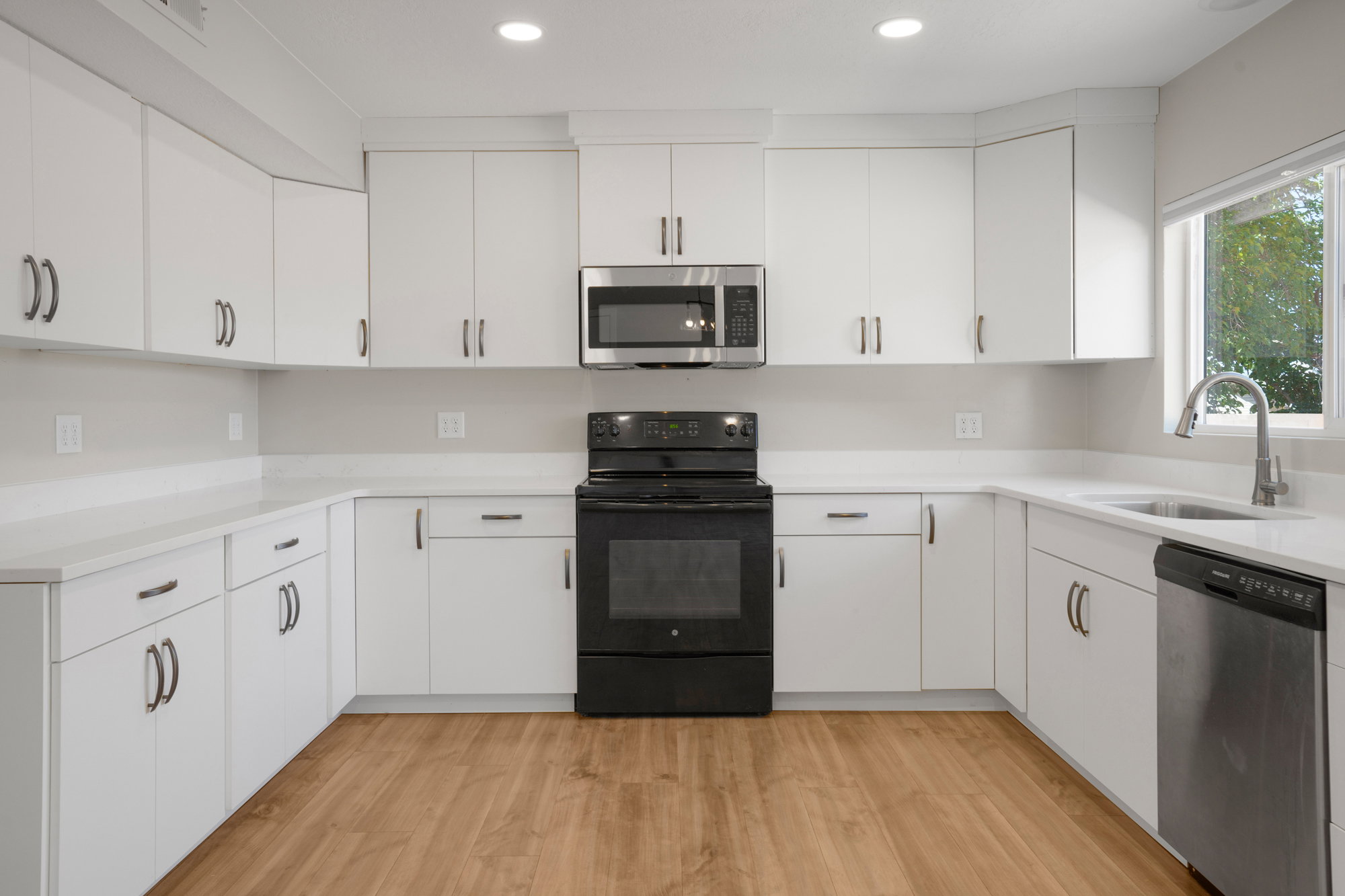 Modern kitchen featuring white cabinetry, light-colored countertops, stainless steel appliances, and wood-finish flooring