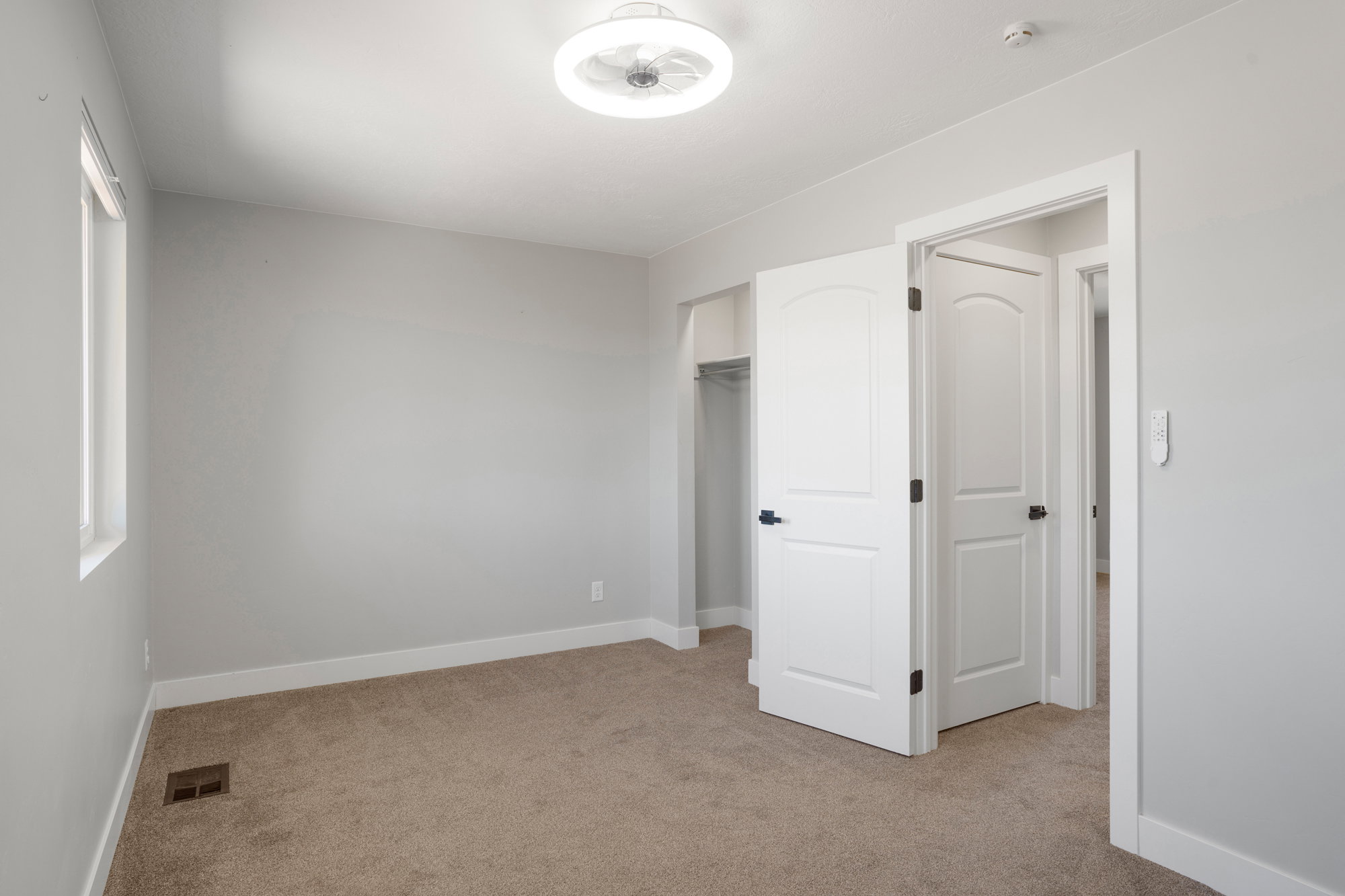 Carpeted room with light gray walls, a flush-mount ceiling light fixture, a window with white trim, and a doorway with a white arched panel door and dark hardware