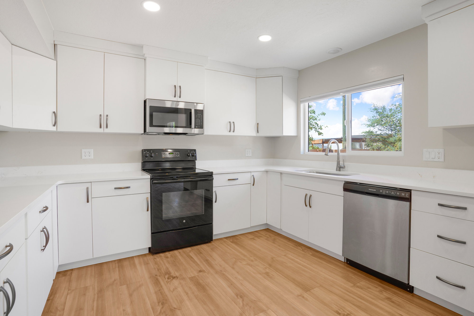 Kitchen featuring white cabinetry, light-toned countertops, wood-finish flooring, stainless steel dishwasher, and an over-the-range microwave