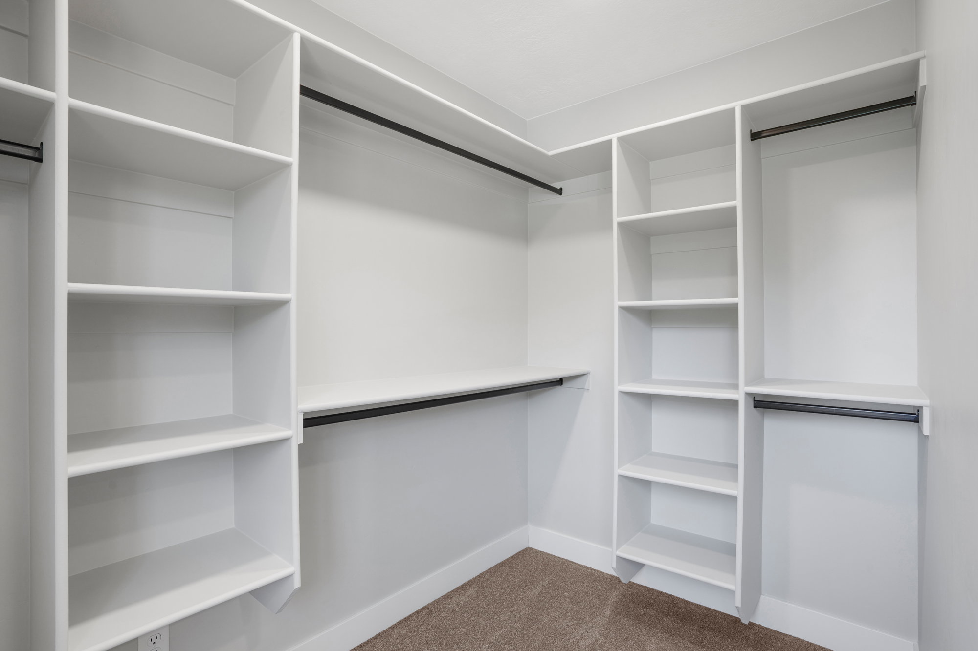 Walk-in closet featuring white built-in shelving, multiple hanging rods, and light brown carpeting