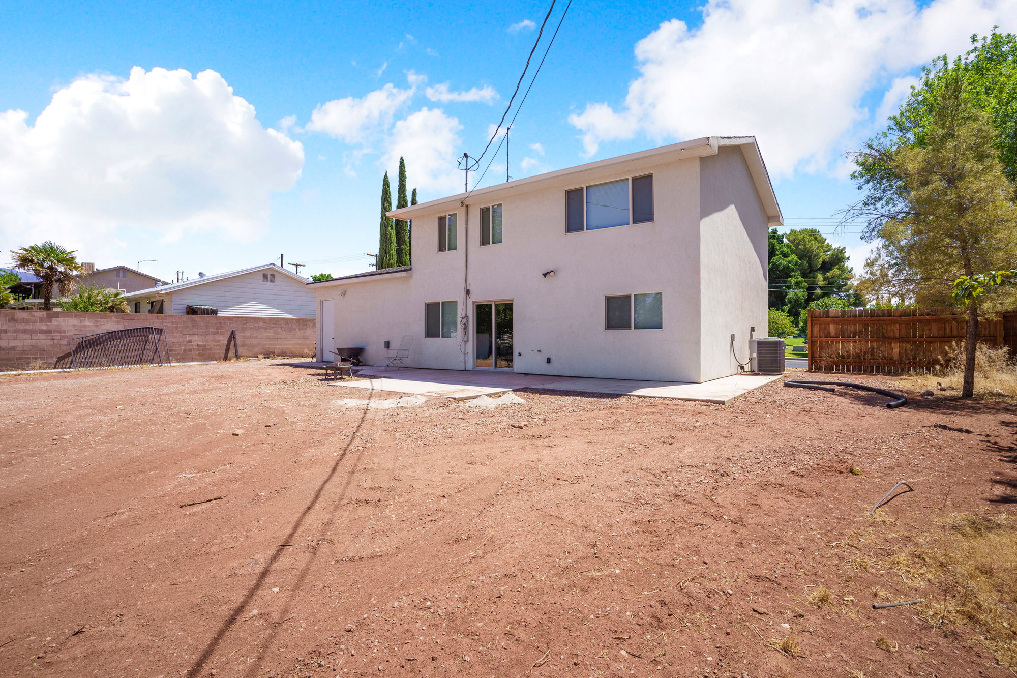 Expansive rear yard featuring a large concrete patio, a privacy fence, and a stucco exterior