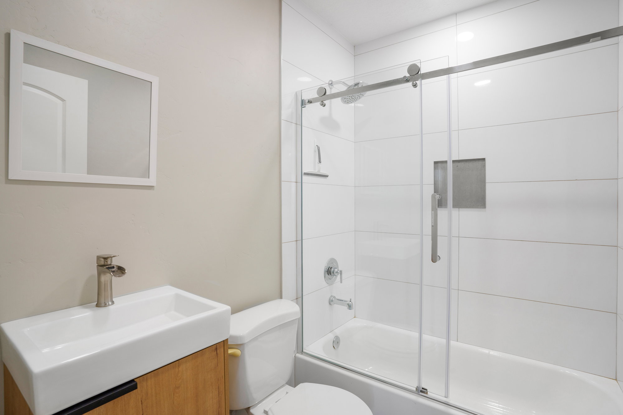 Modern bathroom featuring a single floating vanity with a vessel sink, a brushed nickel faucet, and a shower-over-tub combination with a sliding glass door