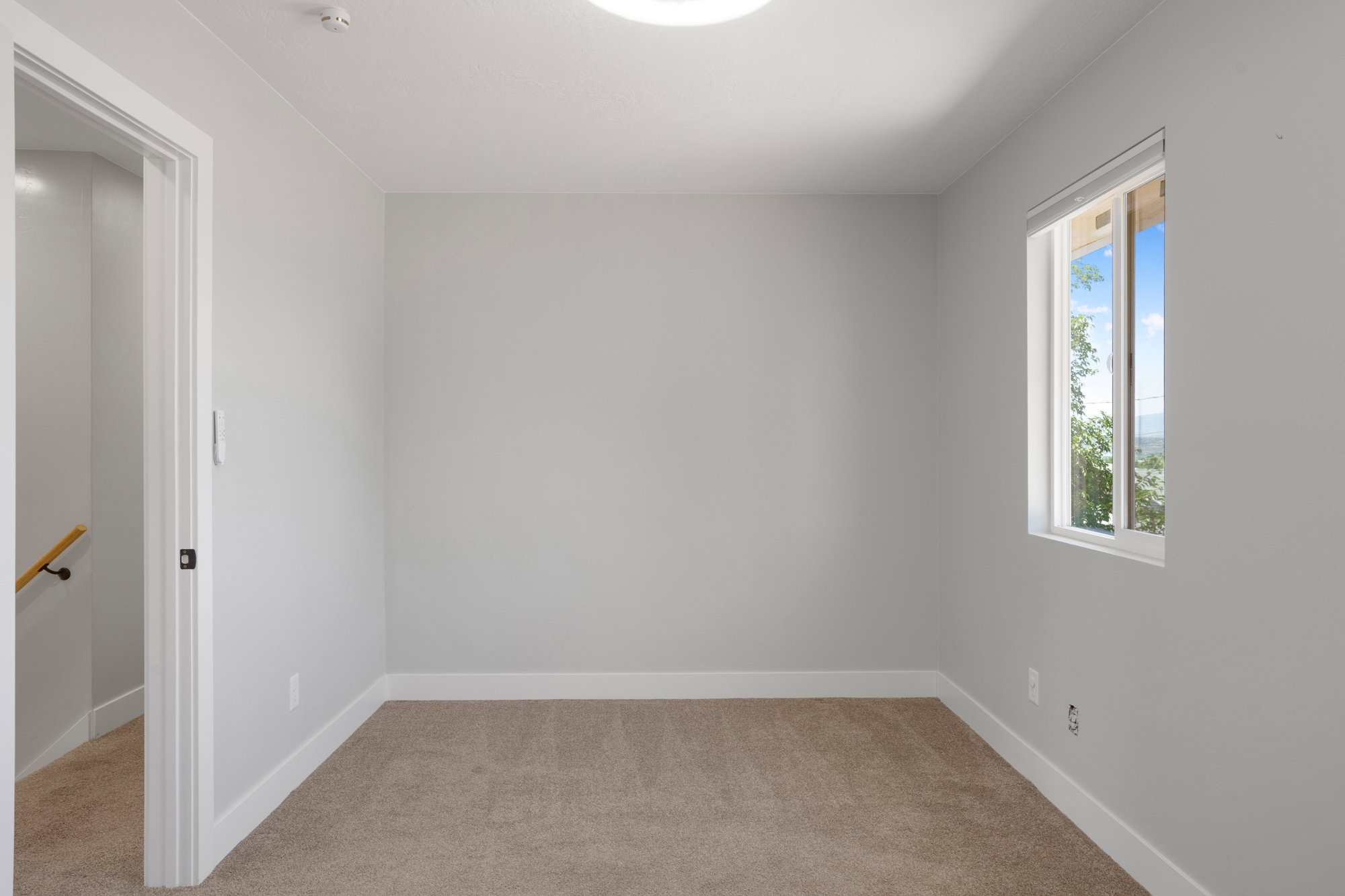 Bright room featuring a window with exterior scenery, light gray walls, white baseboards, and neutral-toned carpeting
