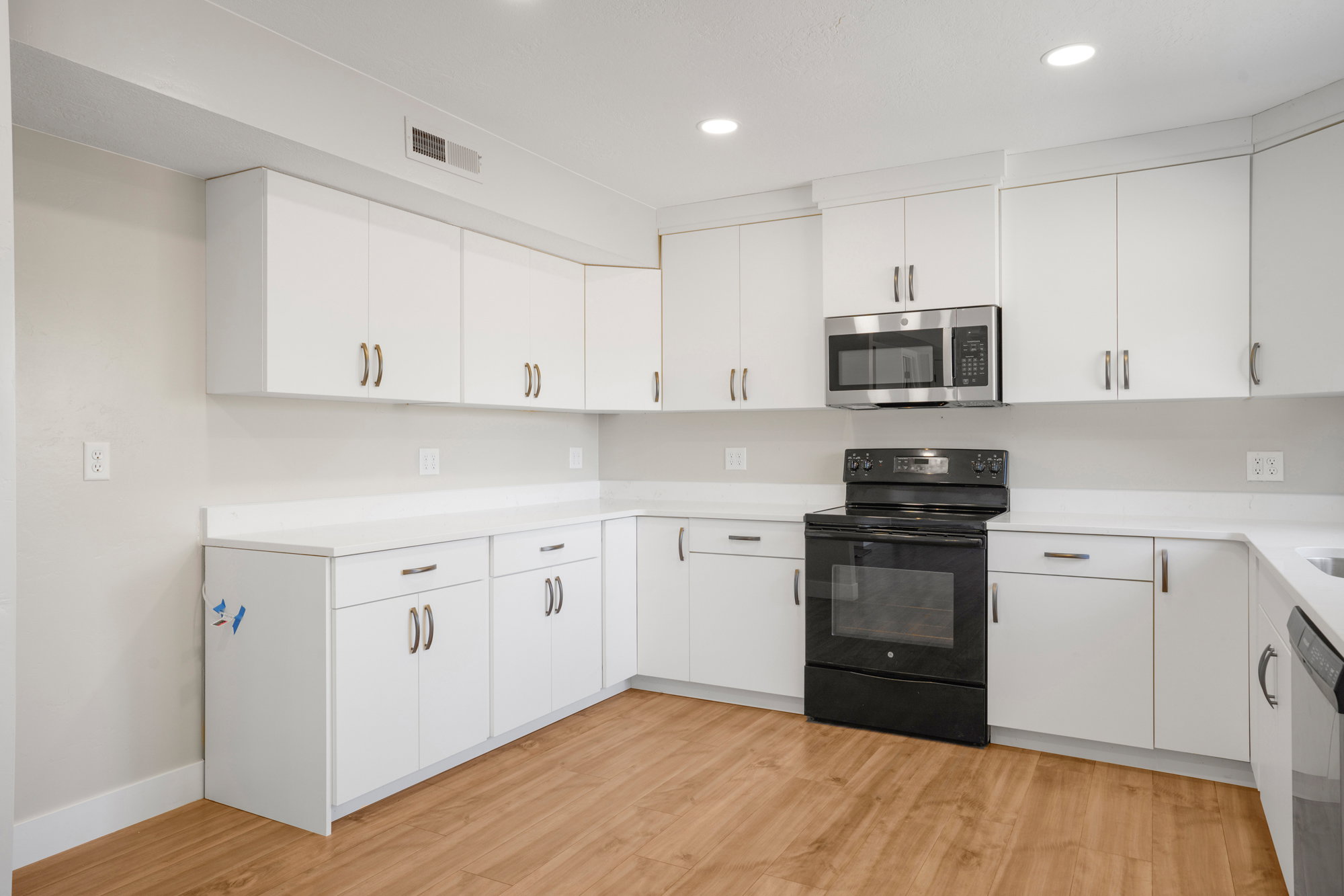 Modern kitchen featuring white cabinetry, light-toned countertops, and wood-finish flooring