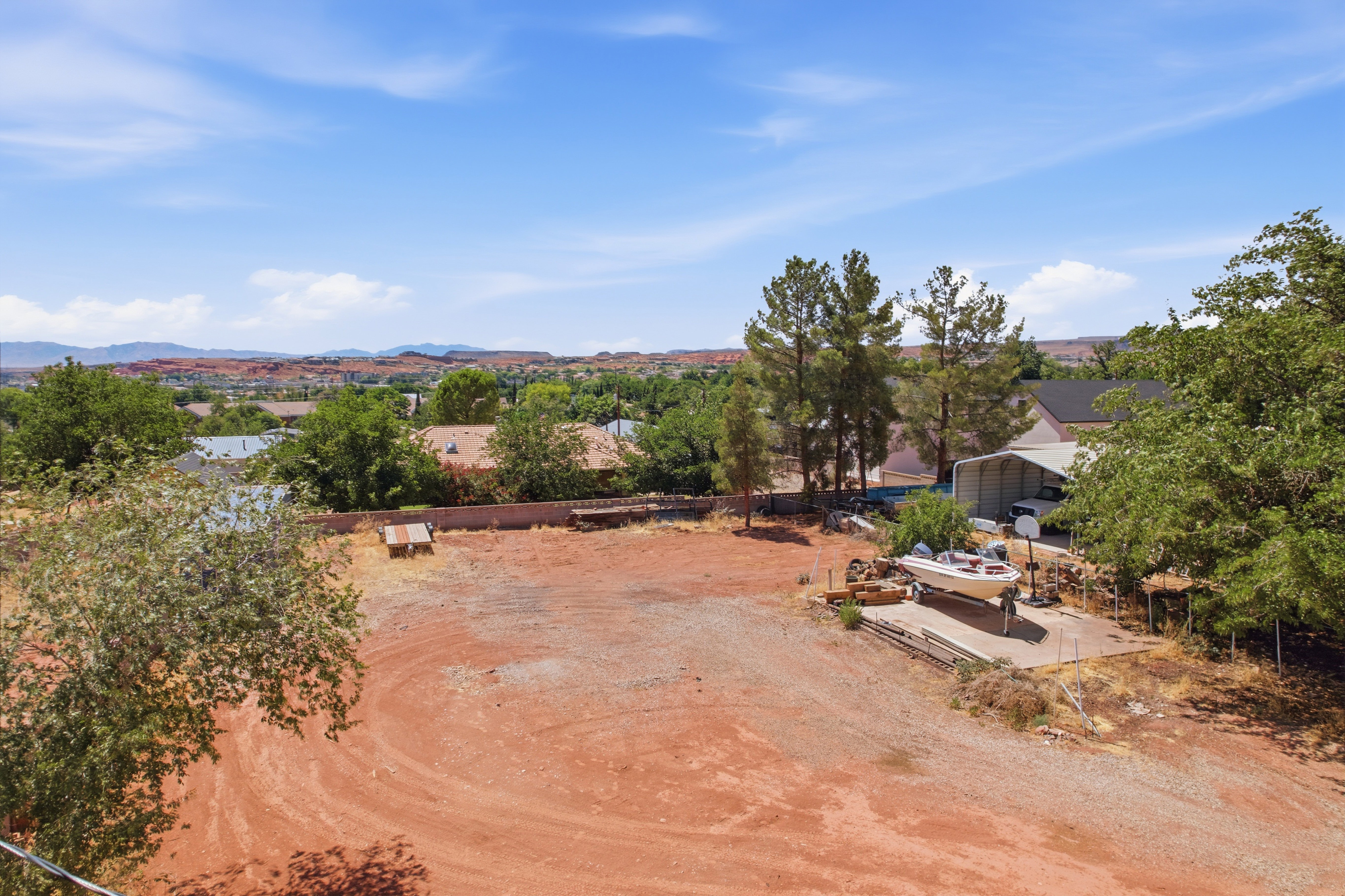 Spacious property featuring an expansive unpaved yard, a covered carport structure, and mature trees providing natural screening