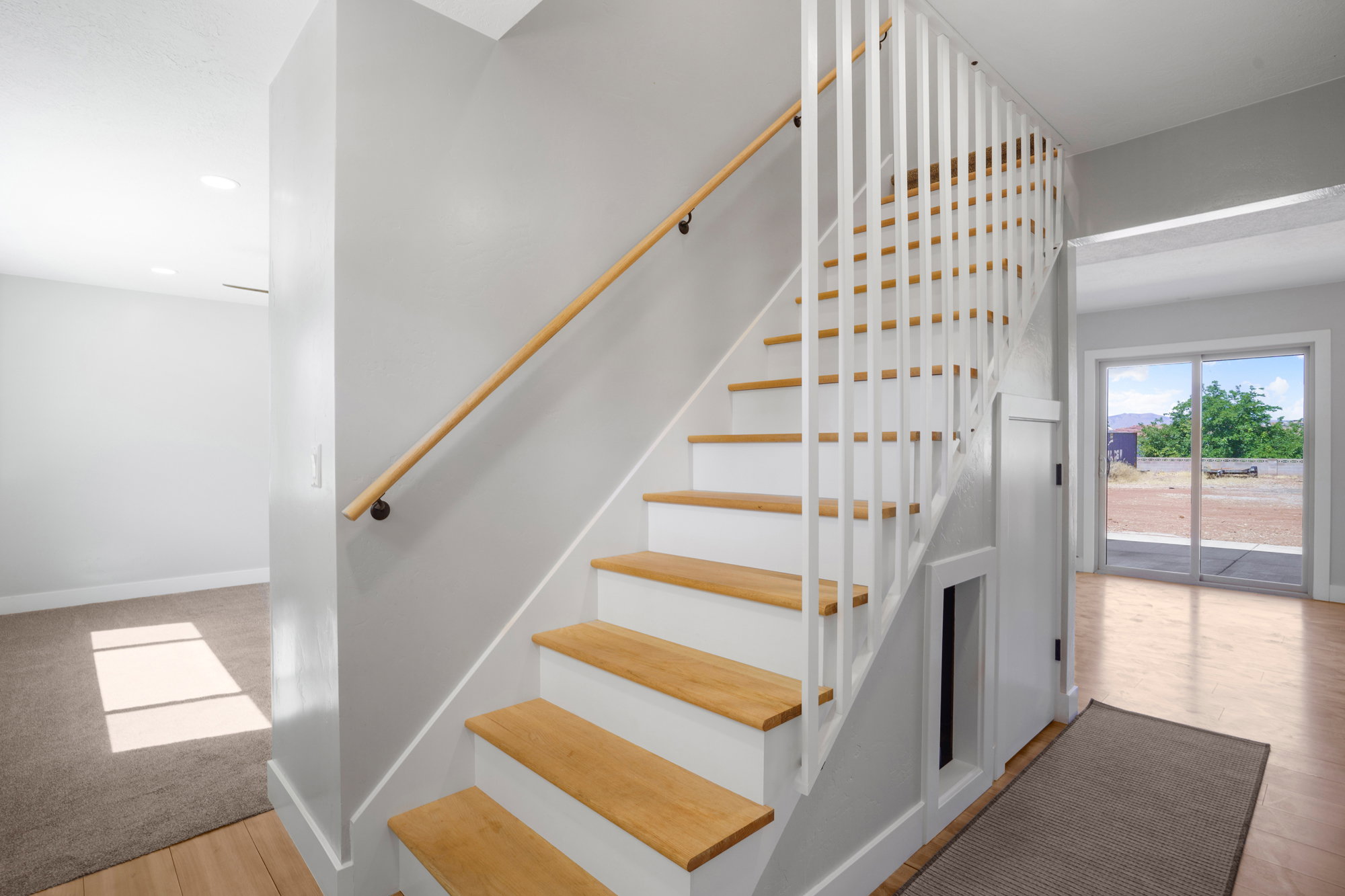 Staircase with light wood treads and white risers, featuring a matching wood handrail and white vertical balusters