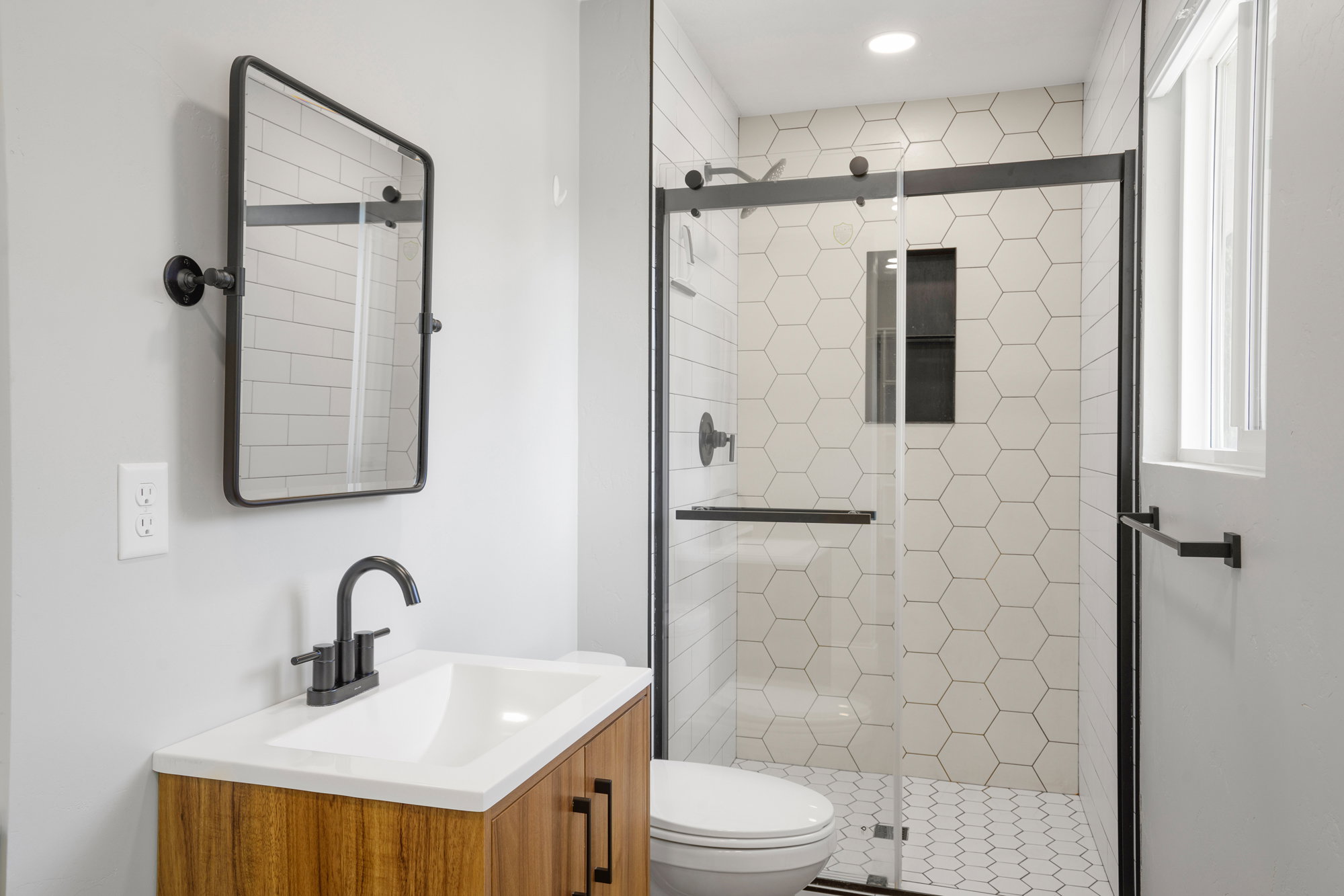 Modern bathroom featuring a wood-finish vanity with an integrated sink, matte black faucet, and a pivoting rectangular mirror