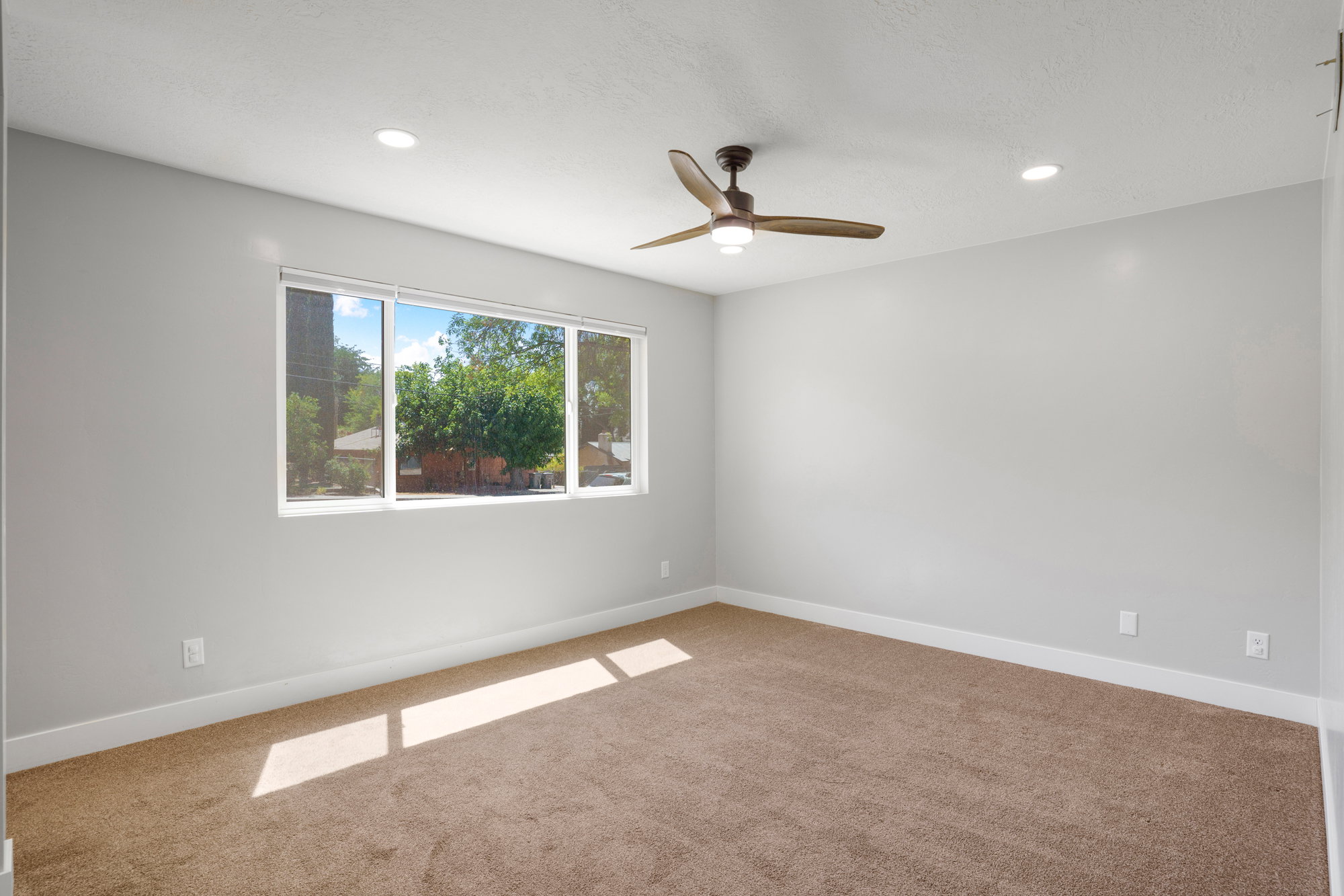 Bright room featuring a large window, recessed lighting, a ceiling fan with integrated light, light gray walls, and brown carpet flooring