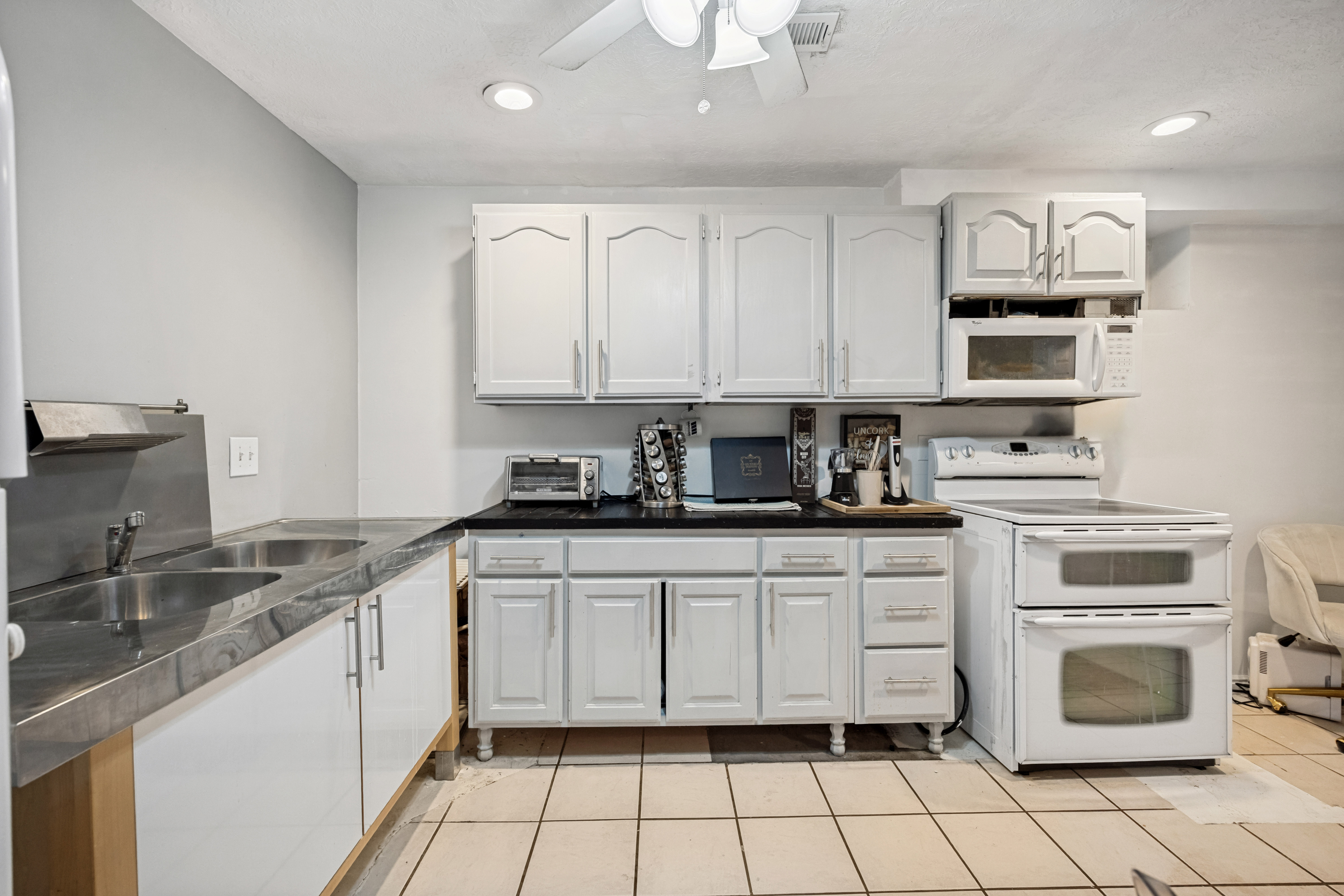 Kitchen featuring white cabinetry, a double basin stainless steel sink, black countertops, and a white electric range with a double oven