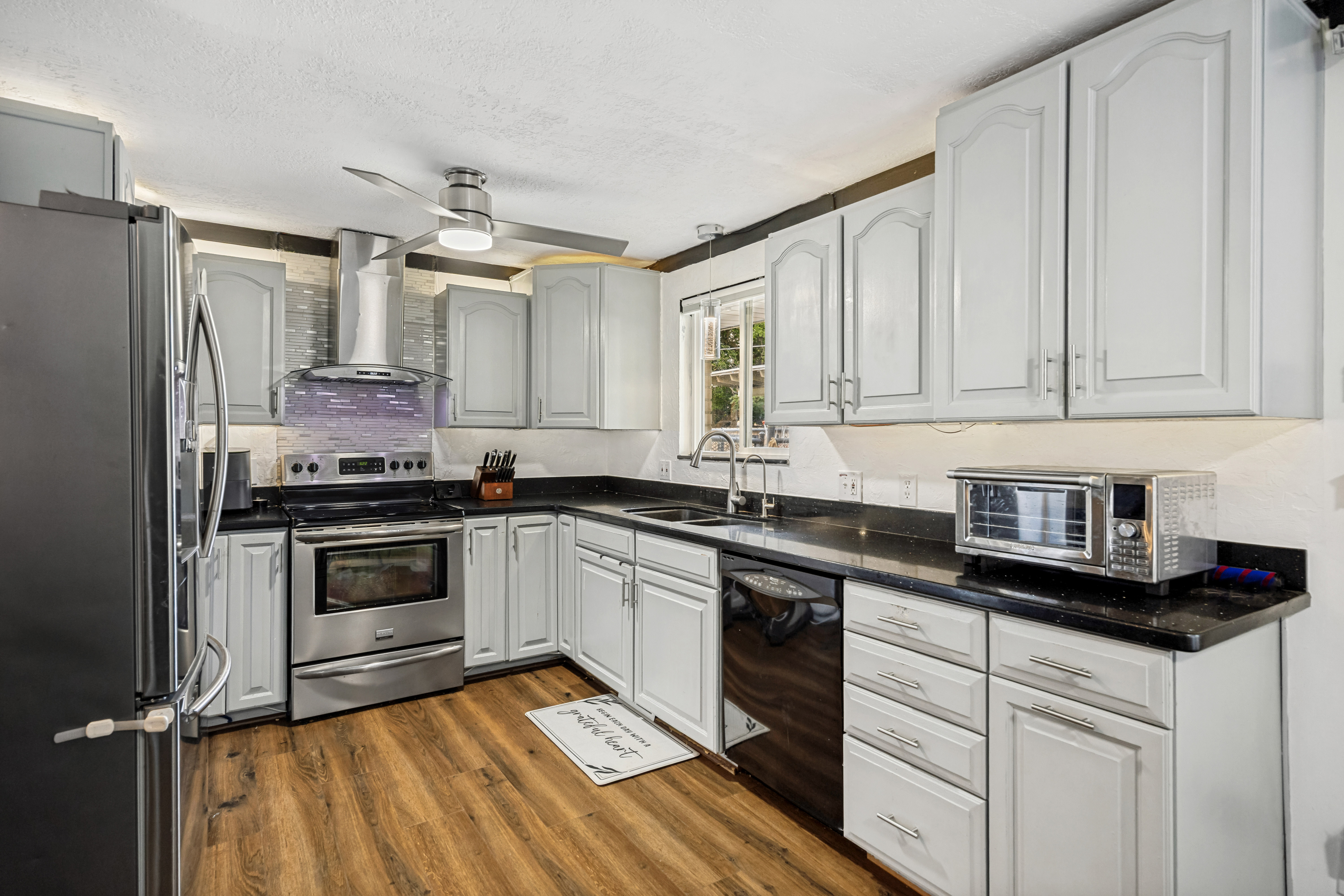 Kitchen featuring wood-finish flooring, light-toned cabinetry, dark countertops, a stainless steel range with a ventilation hood, and a ceiling fan