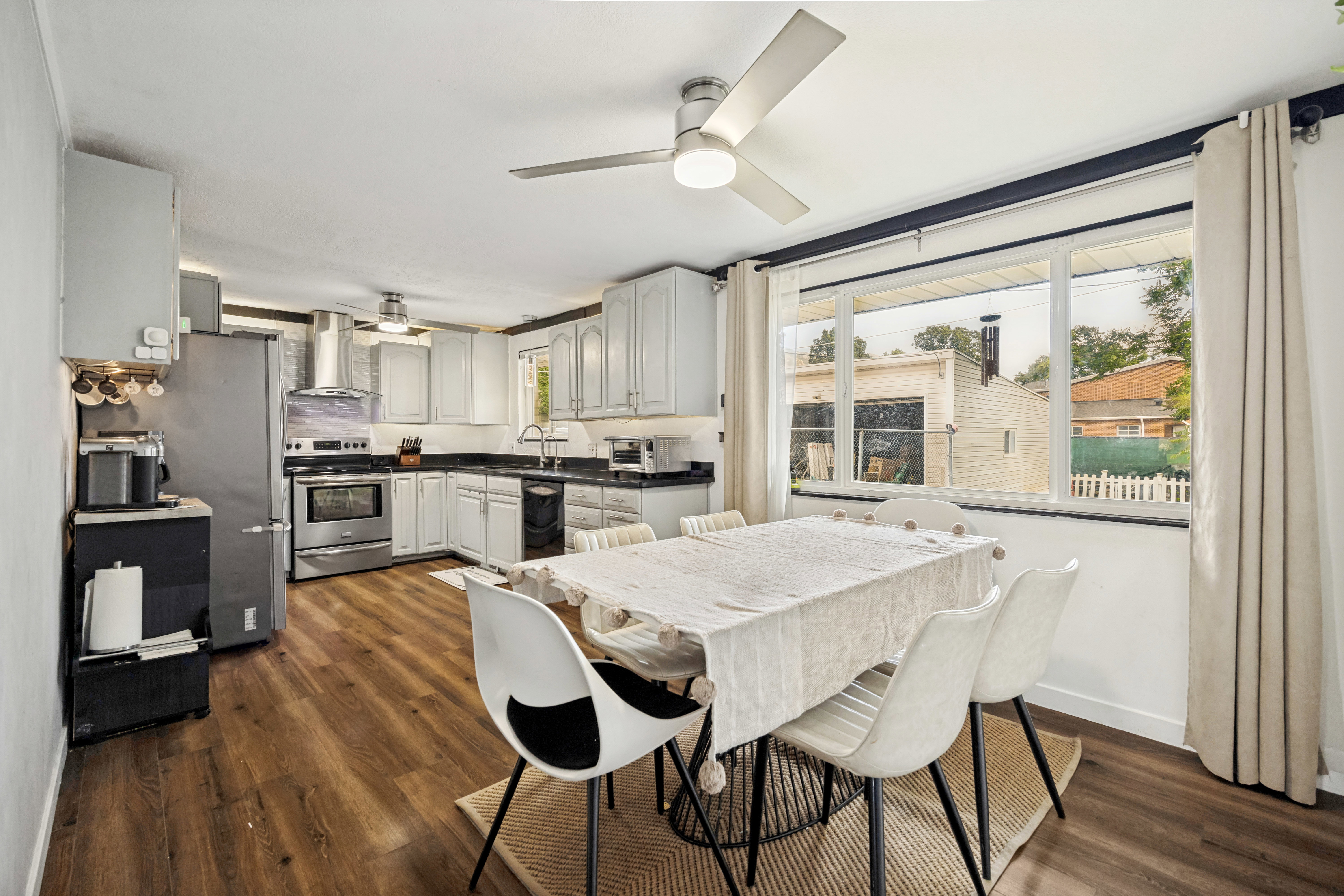 Open-concept kitchen and dining area featuring wood-finish flooring, white cabinetry, dark countertops, and stainless steel appliances