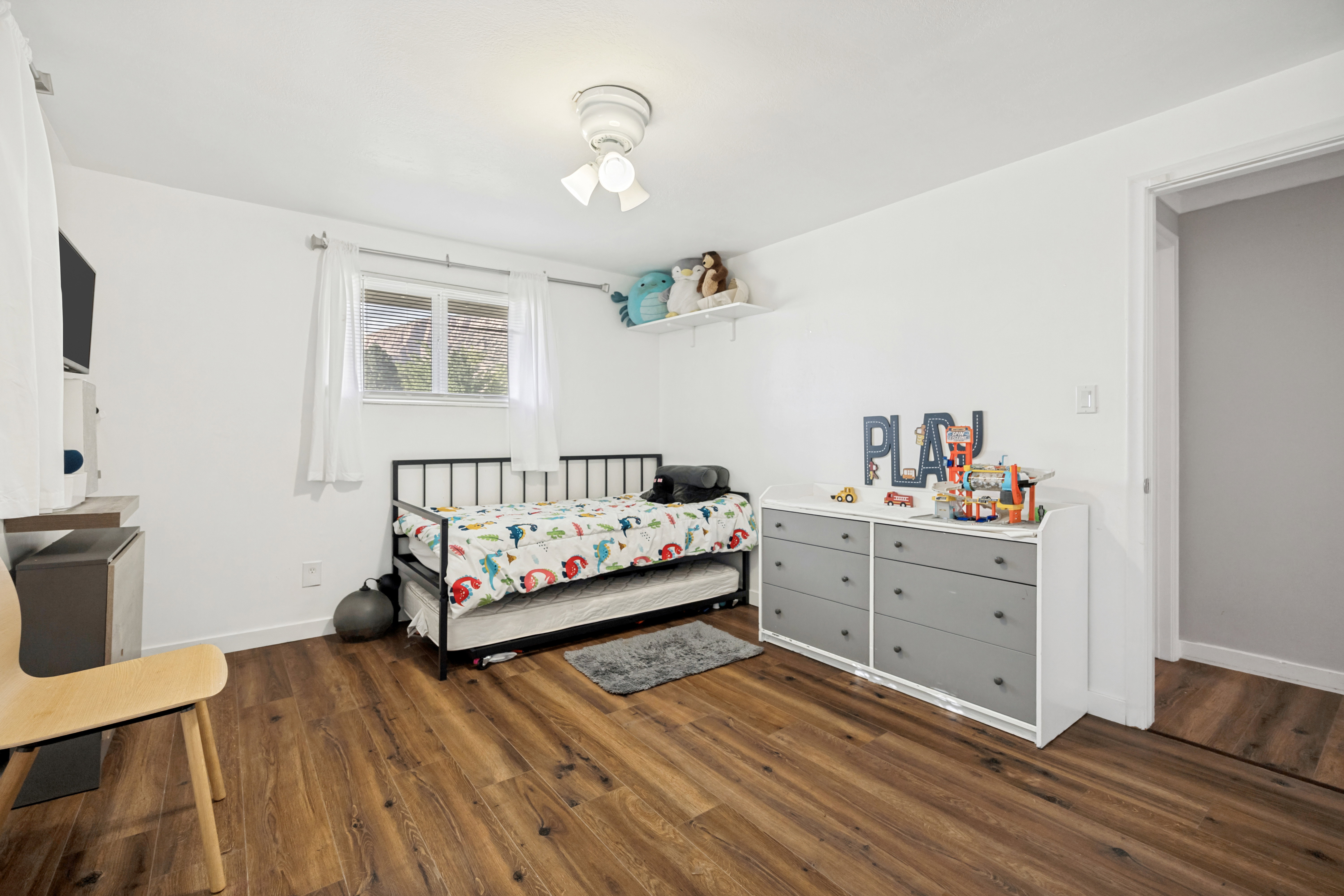 Bright room featuring wood-finish flooring, white walls, and a window with white curtains