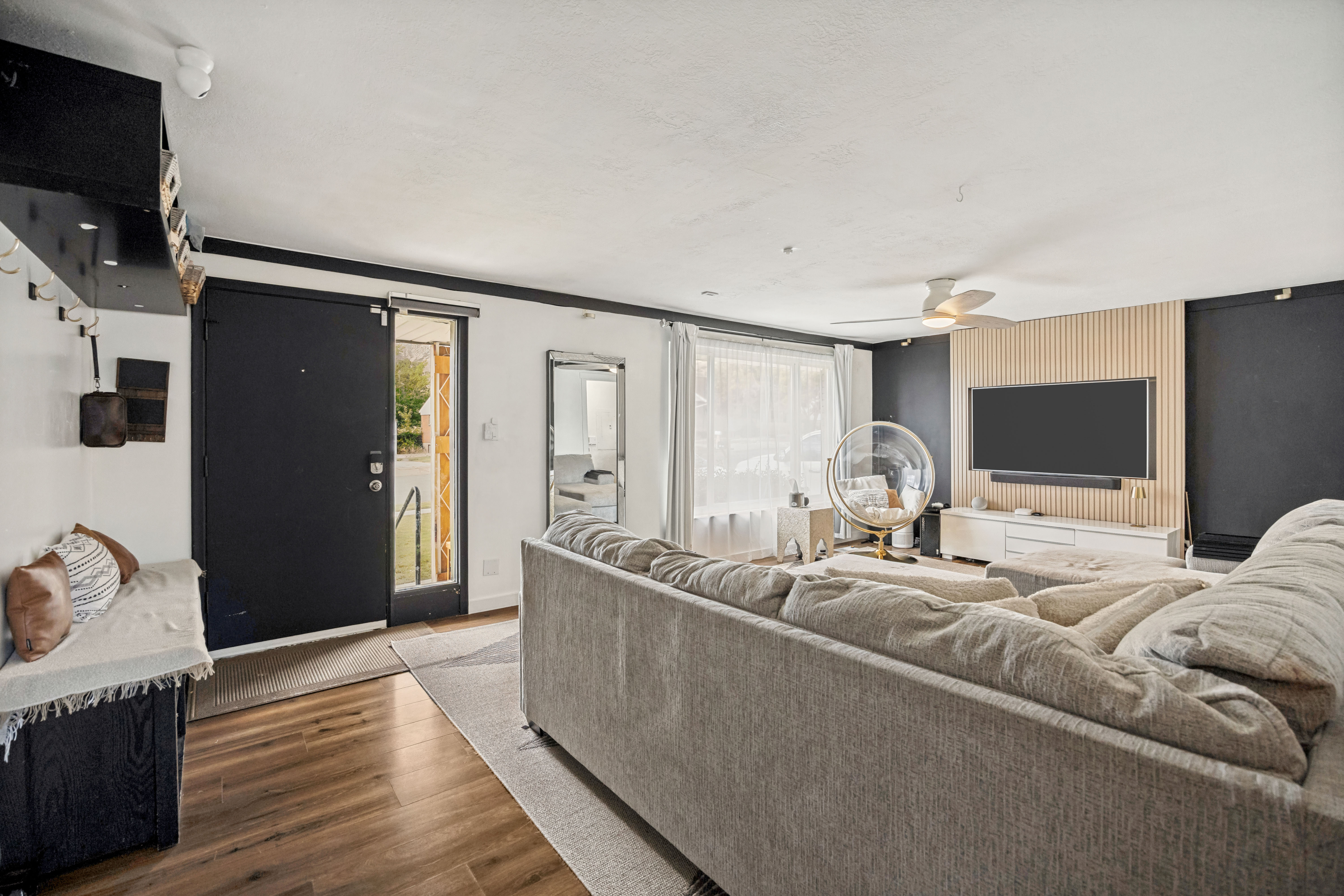 Open-concept living space featuring wood-finish flooring, a contemporary ceiling fan, and an accent wall with vertical wood paneling