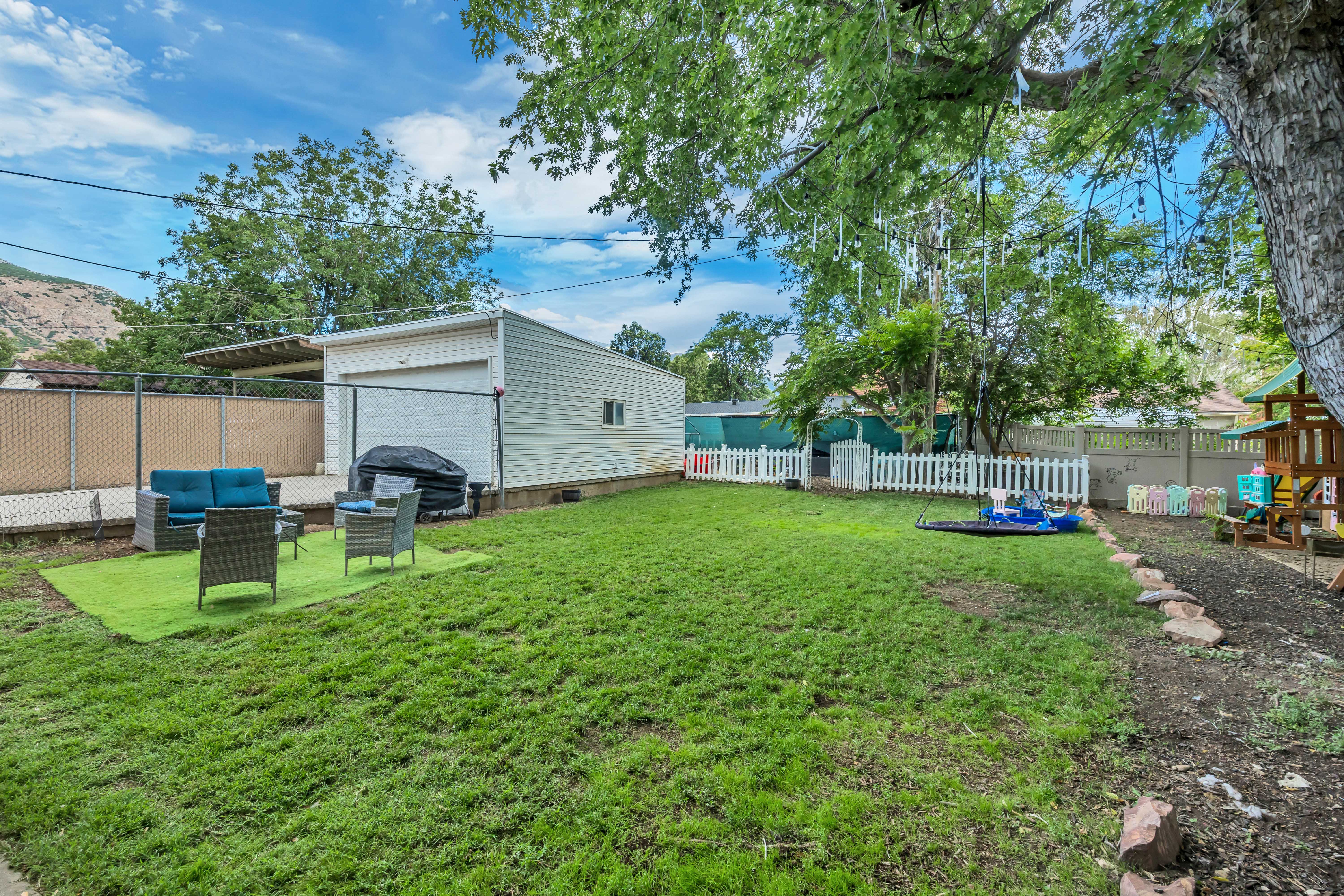 Expansive backyard featuring a manicured lawn, detached garage, and a covered patio area