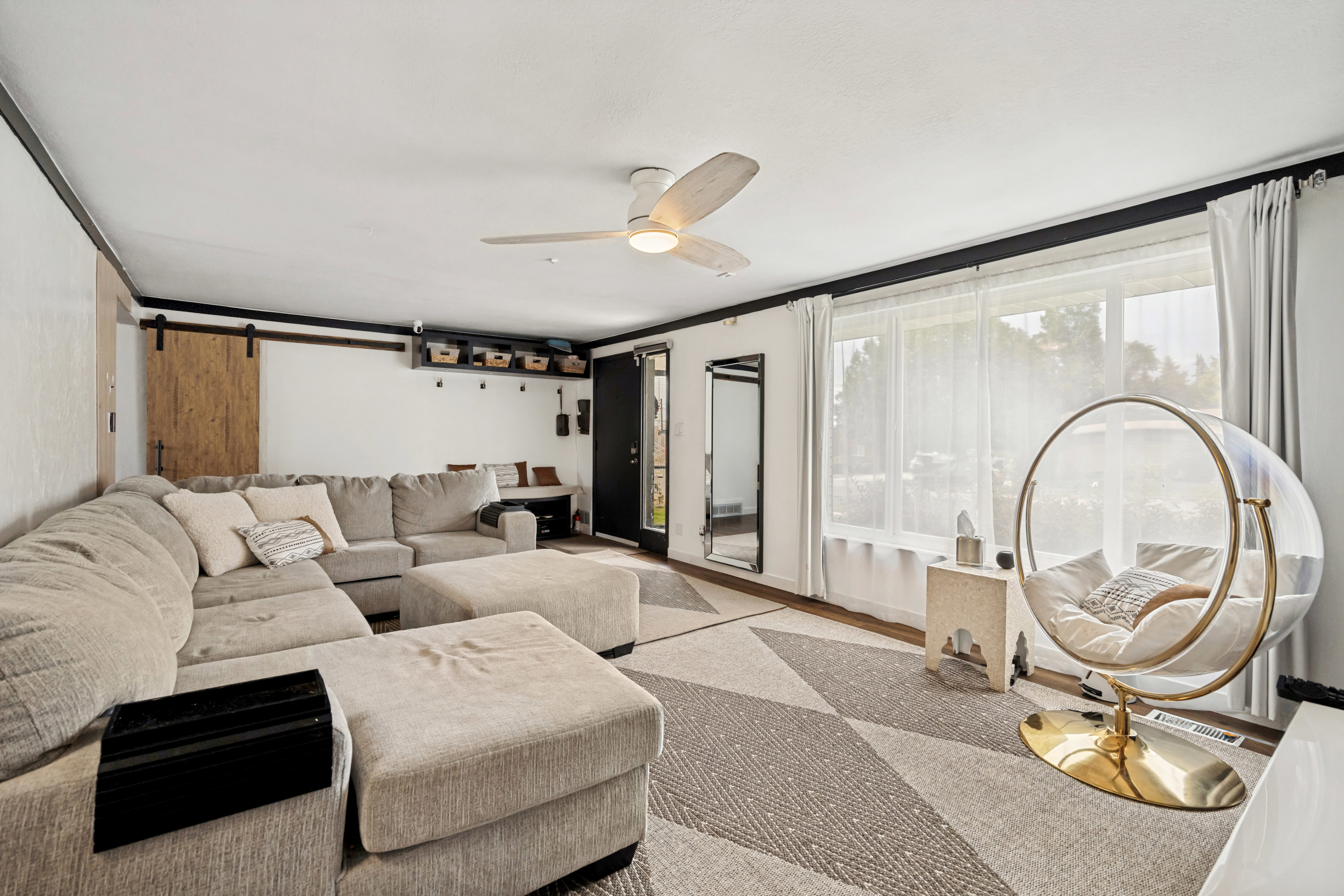 Spacious living area featuring expansive windows, wood-finish flooring, and a ceiling fan with integrated lighting
