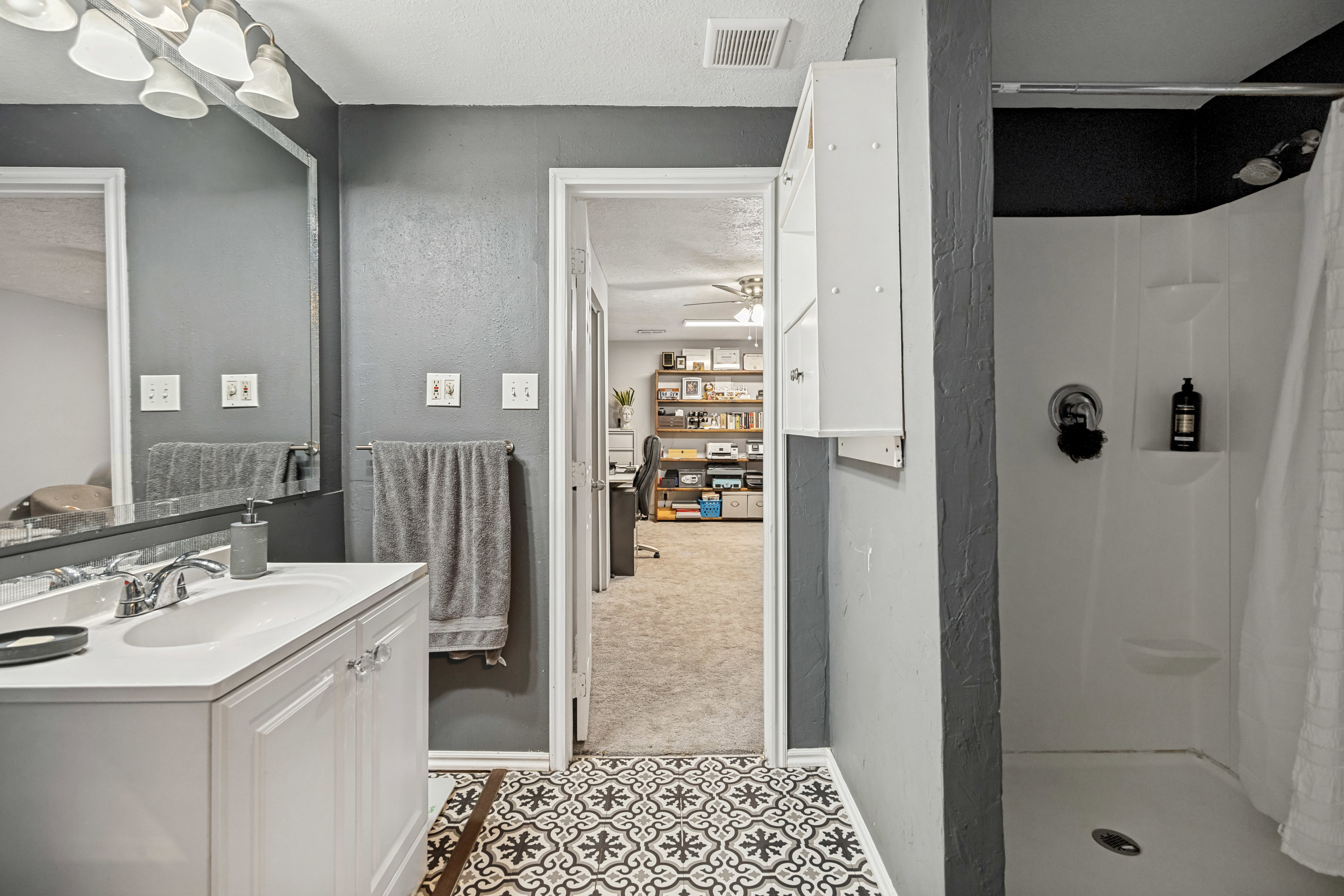 Modern bathroom featuring a white single vanity with a chrome faucet, a large wall-mounted mirror, and decorative patterned floor tiles