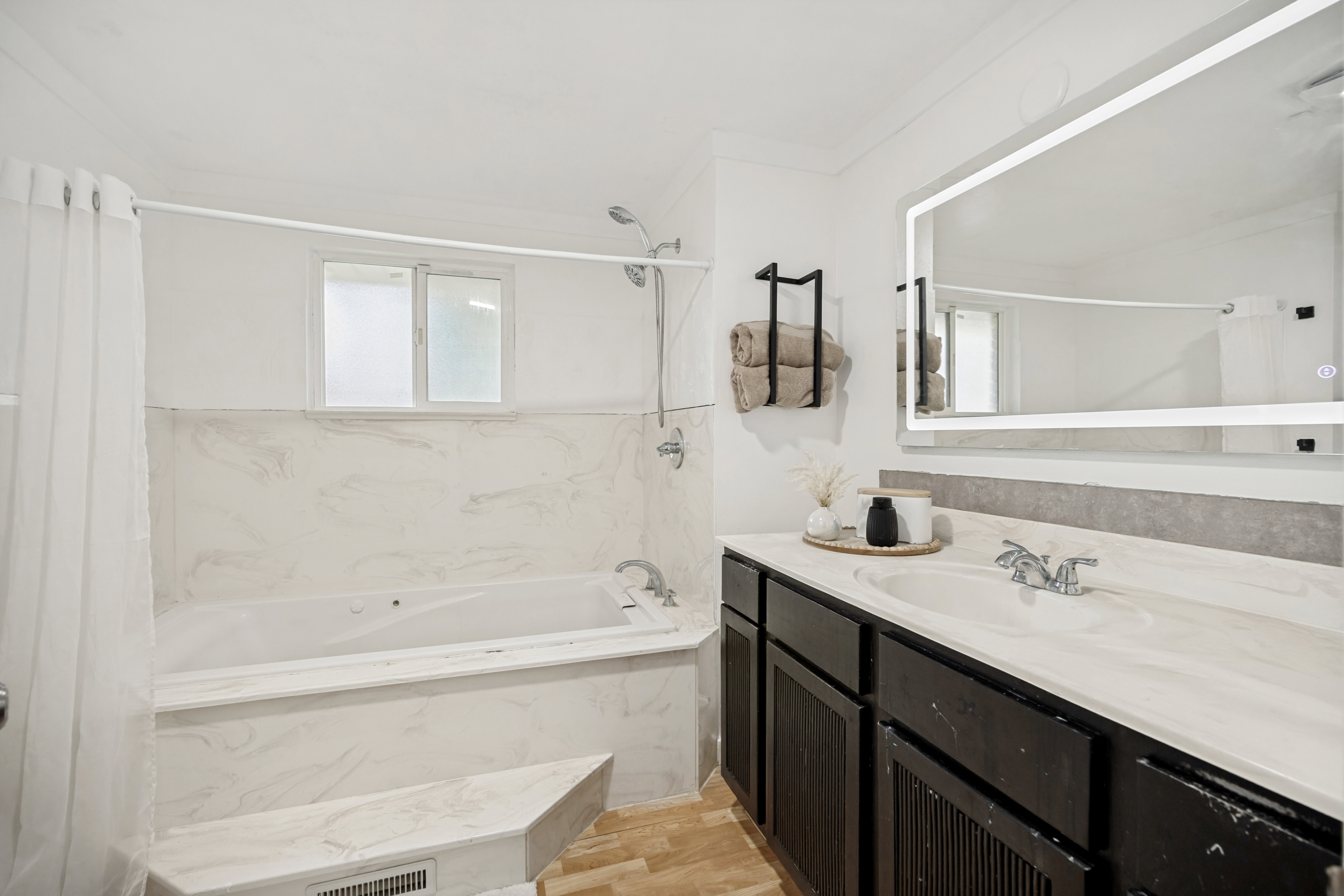 Contemporary bathroom featuring a built-in tub with marble-look surround, a dark wood-finish vanity, a single undermount sink, and an illuminated mirror
