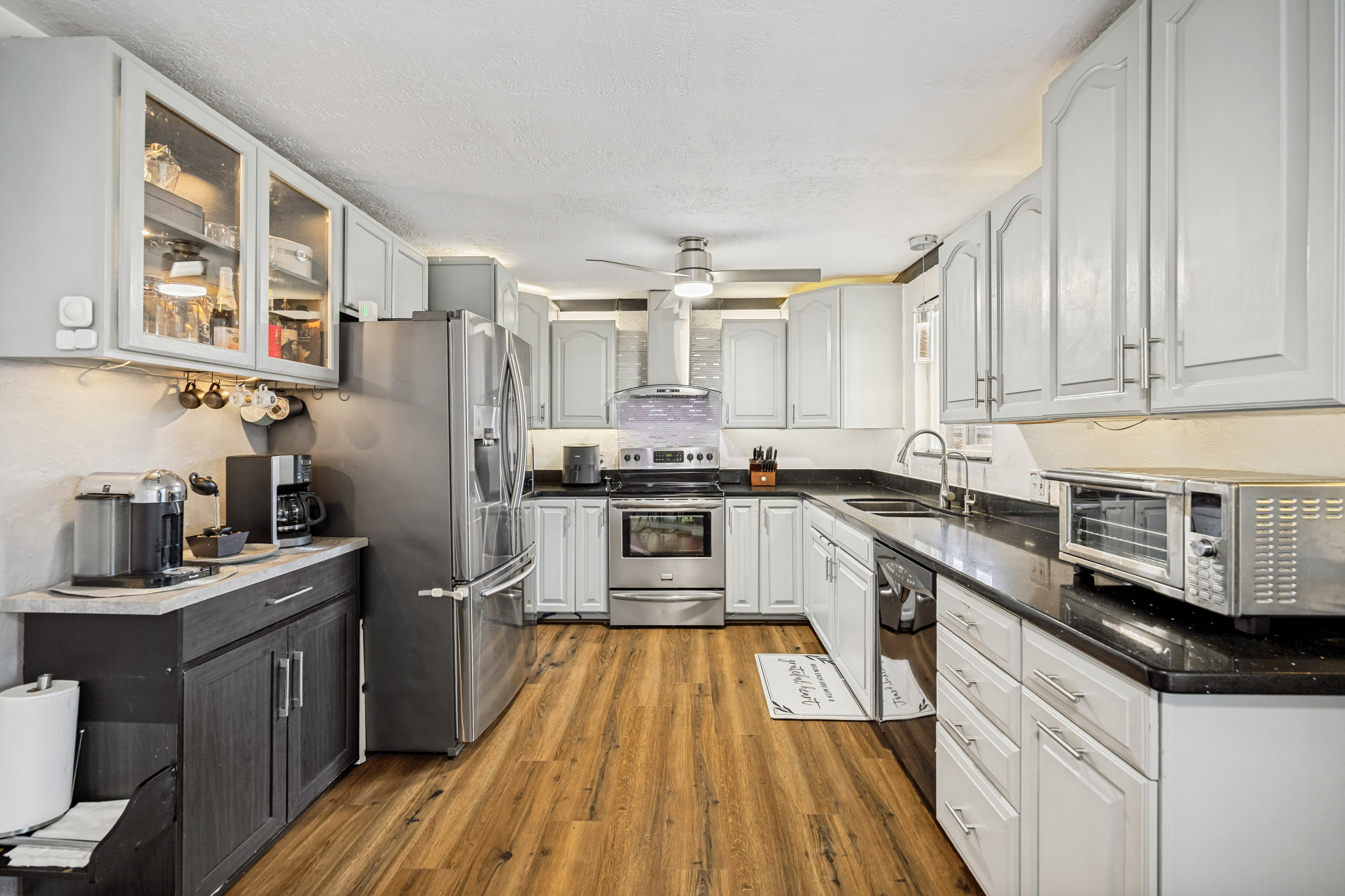 Kitchen featuring wood-finish flooring, white cabinetry with silver hardware, dark countertops, and stainless steel appliances
