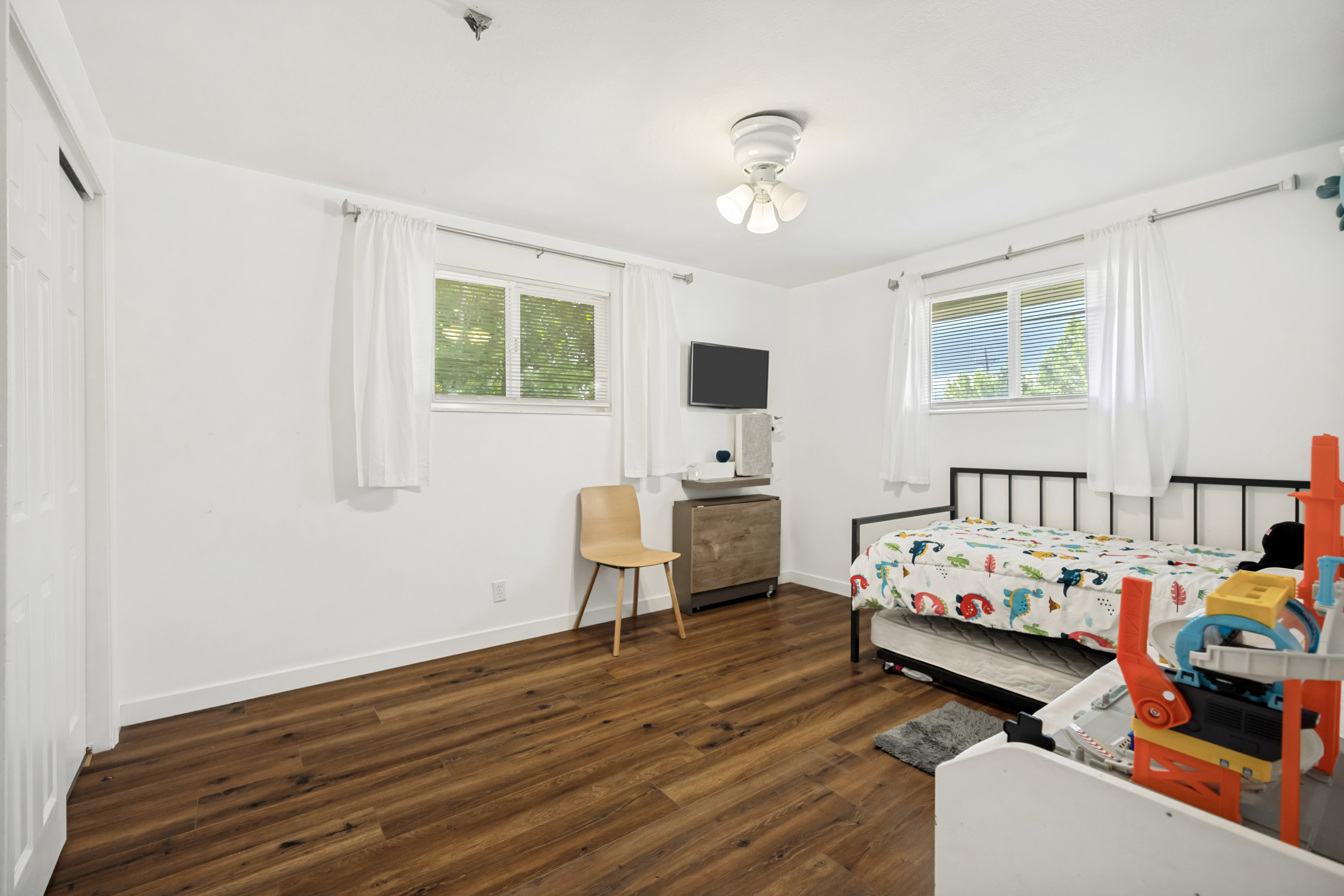 Bright room featuring wood-finish flooring, white walls, and a ceiling fan