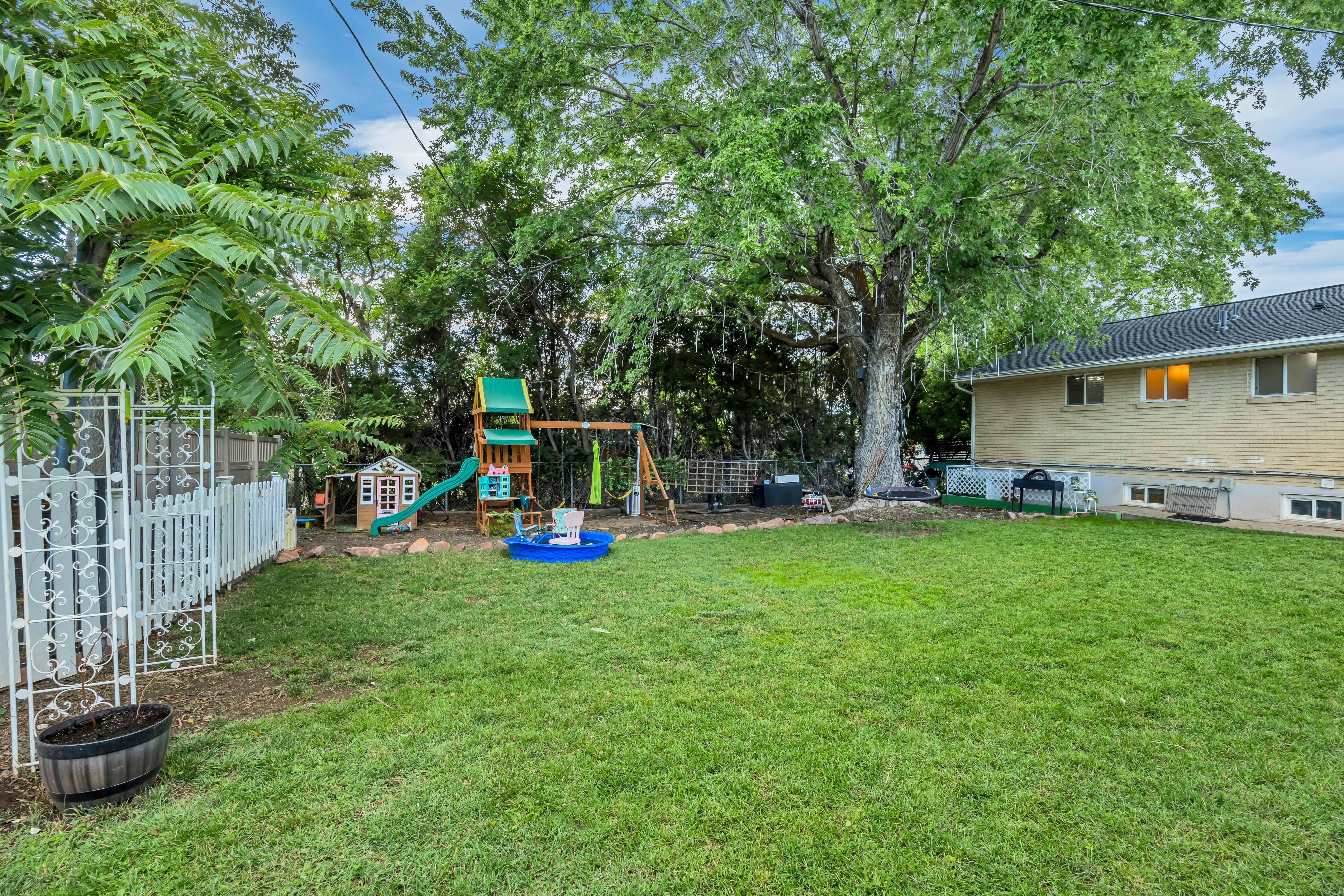 Expansive backyard featuring a lush lawn, mature shade trees, and a white picket fence