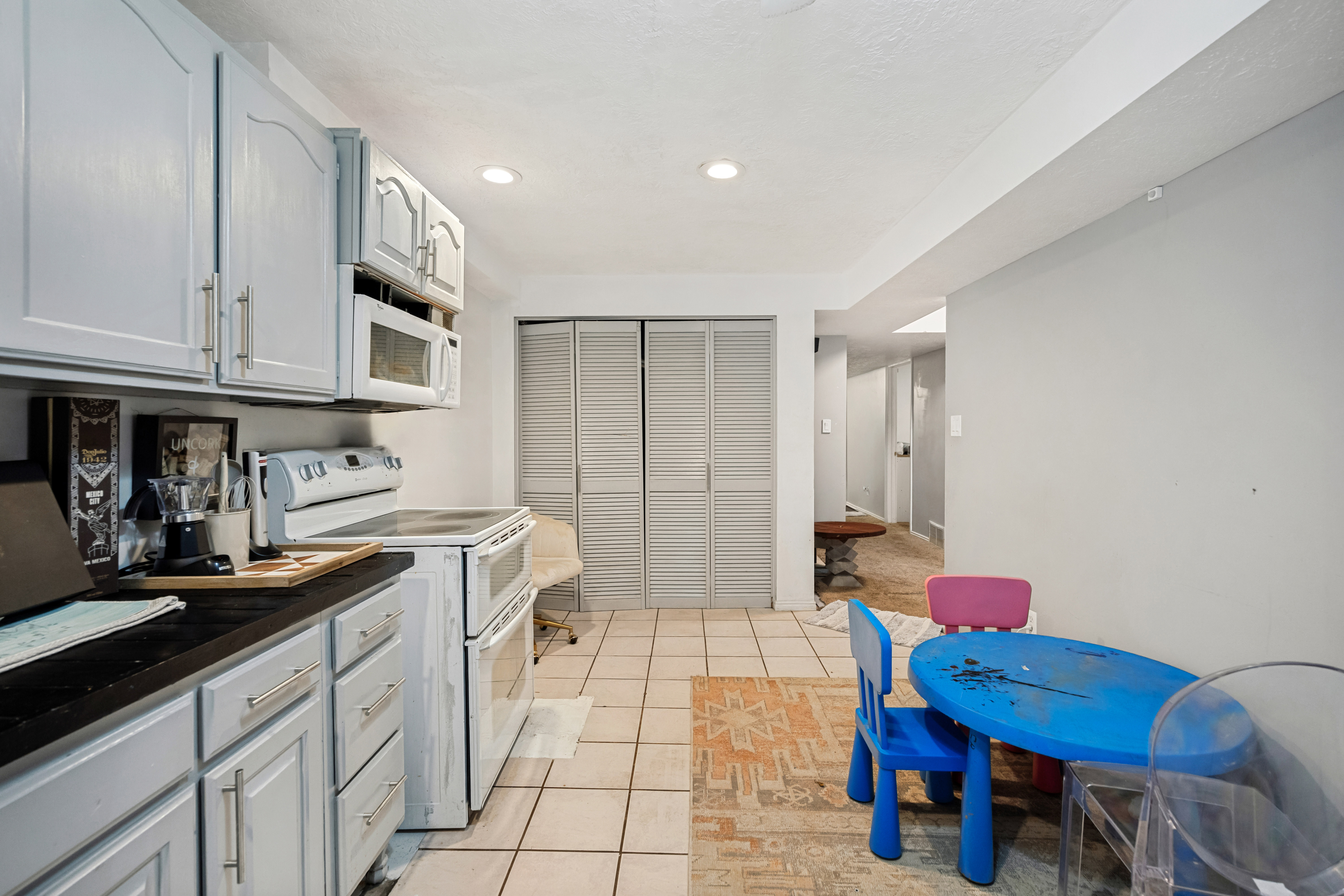 Kitchen featuring light gray cabinetry with brushed nickel hardware, a black countertop, white appliances, and recessed lighting