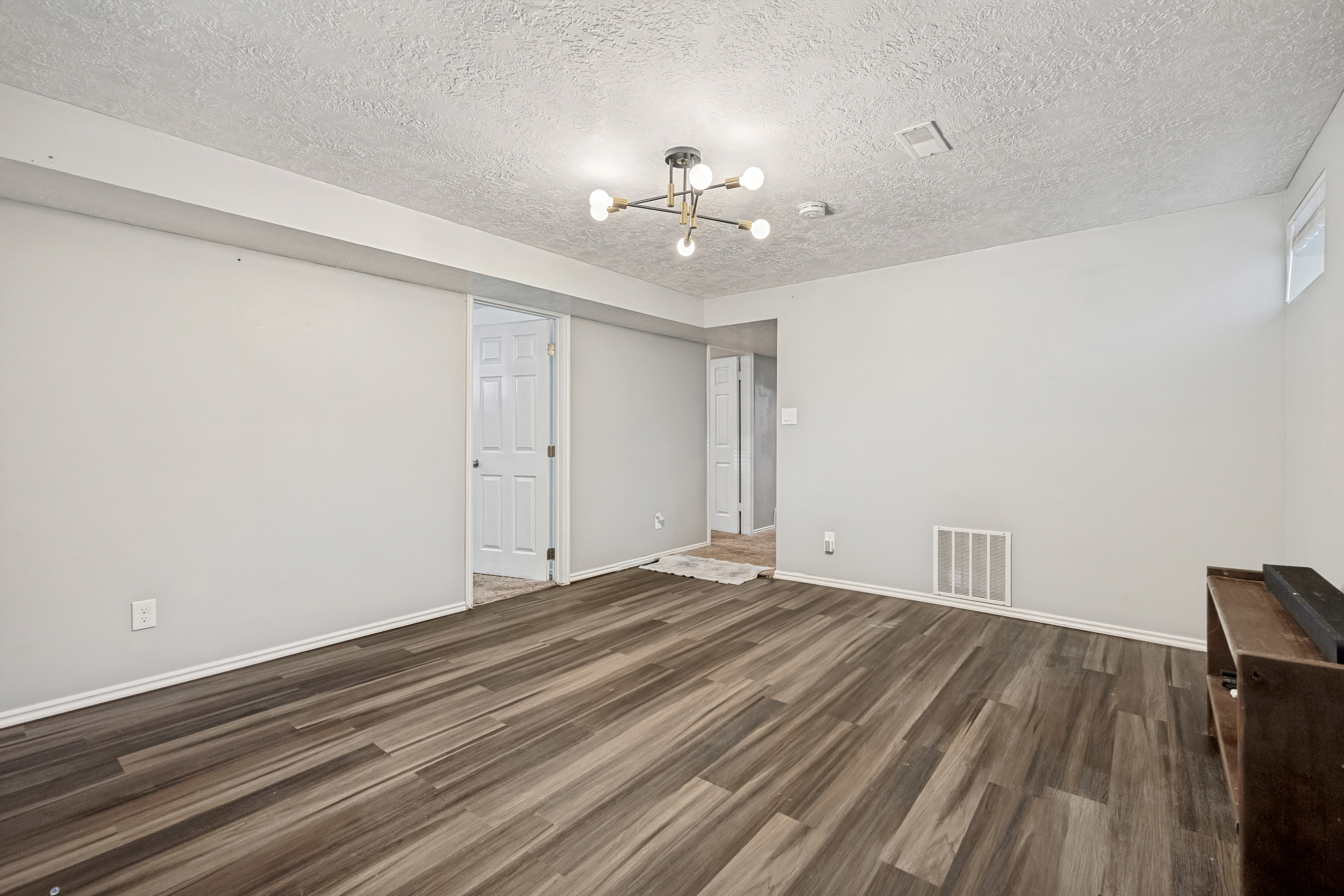Versatile room featuring wood-finish flooring, light gray wall paint, and a modern ceiling light fixture