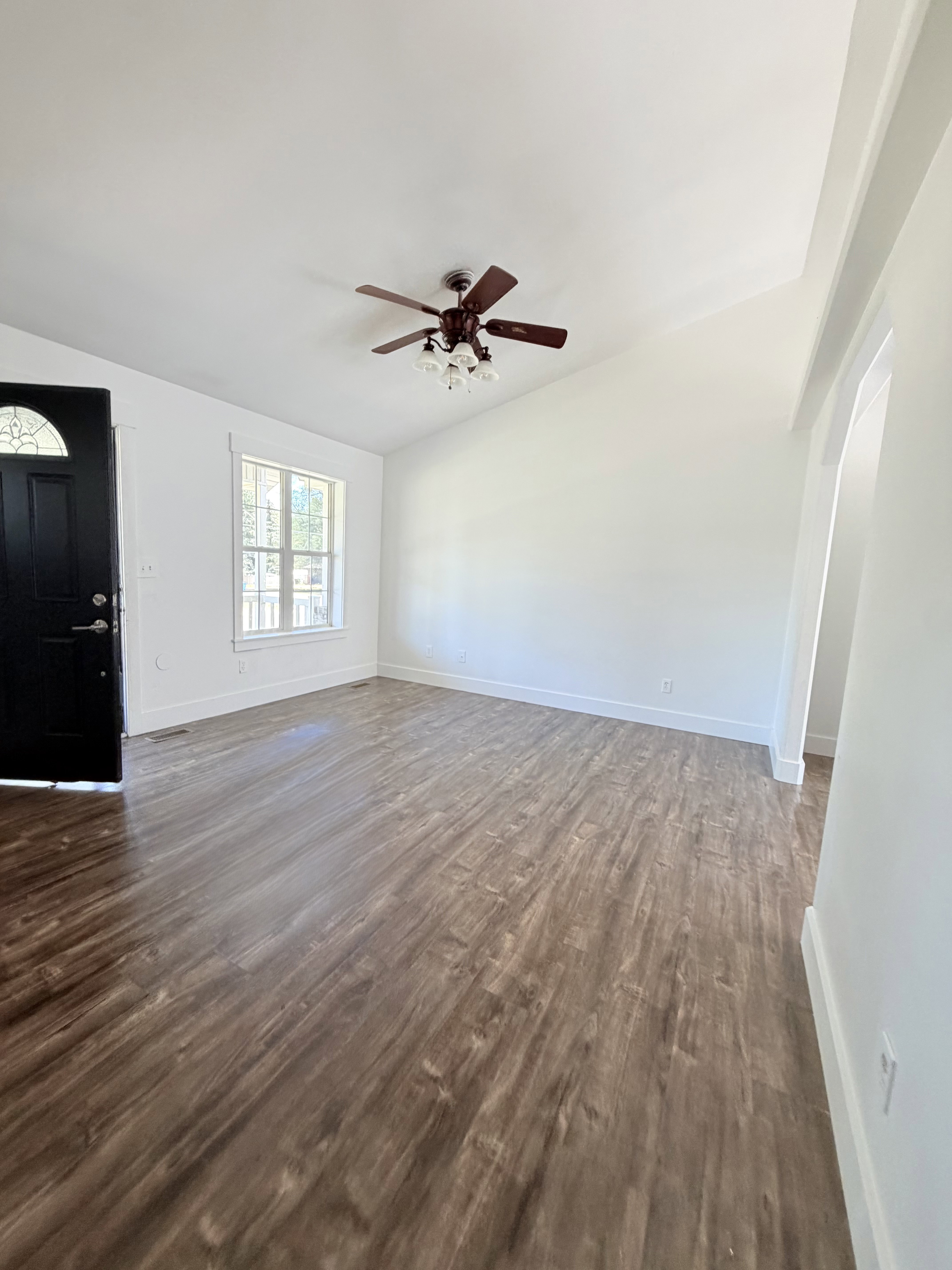Open-concept living space with wood-finish flooring, vaulted ceilings, and a ceiling fan with integrated lighting