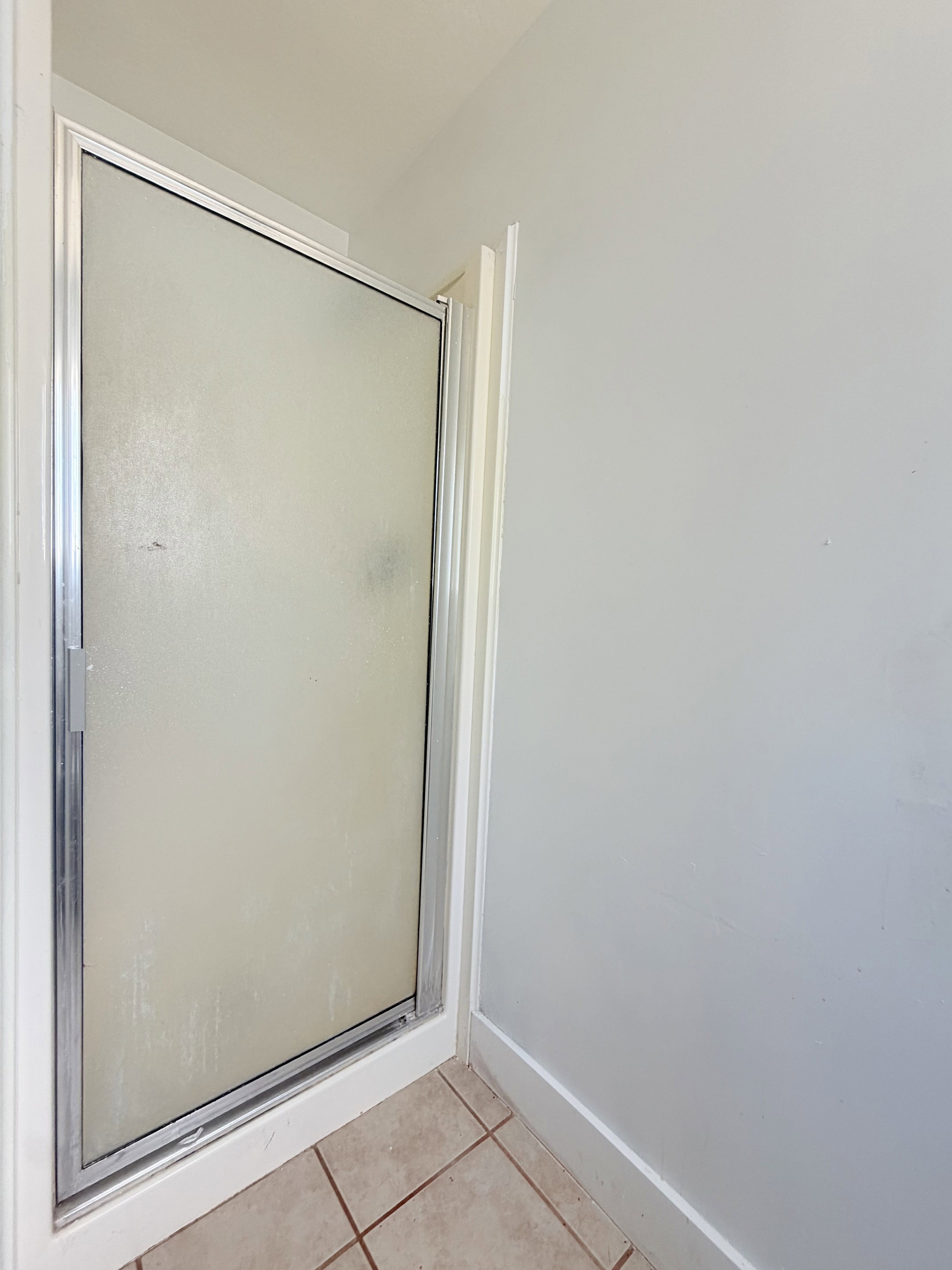 Enclosed shower stall with a frosted glass door and a metal frame, set on light-toned tile flooring