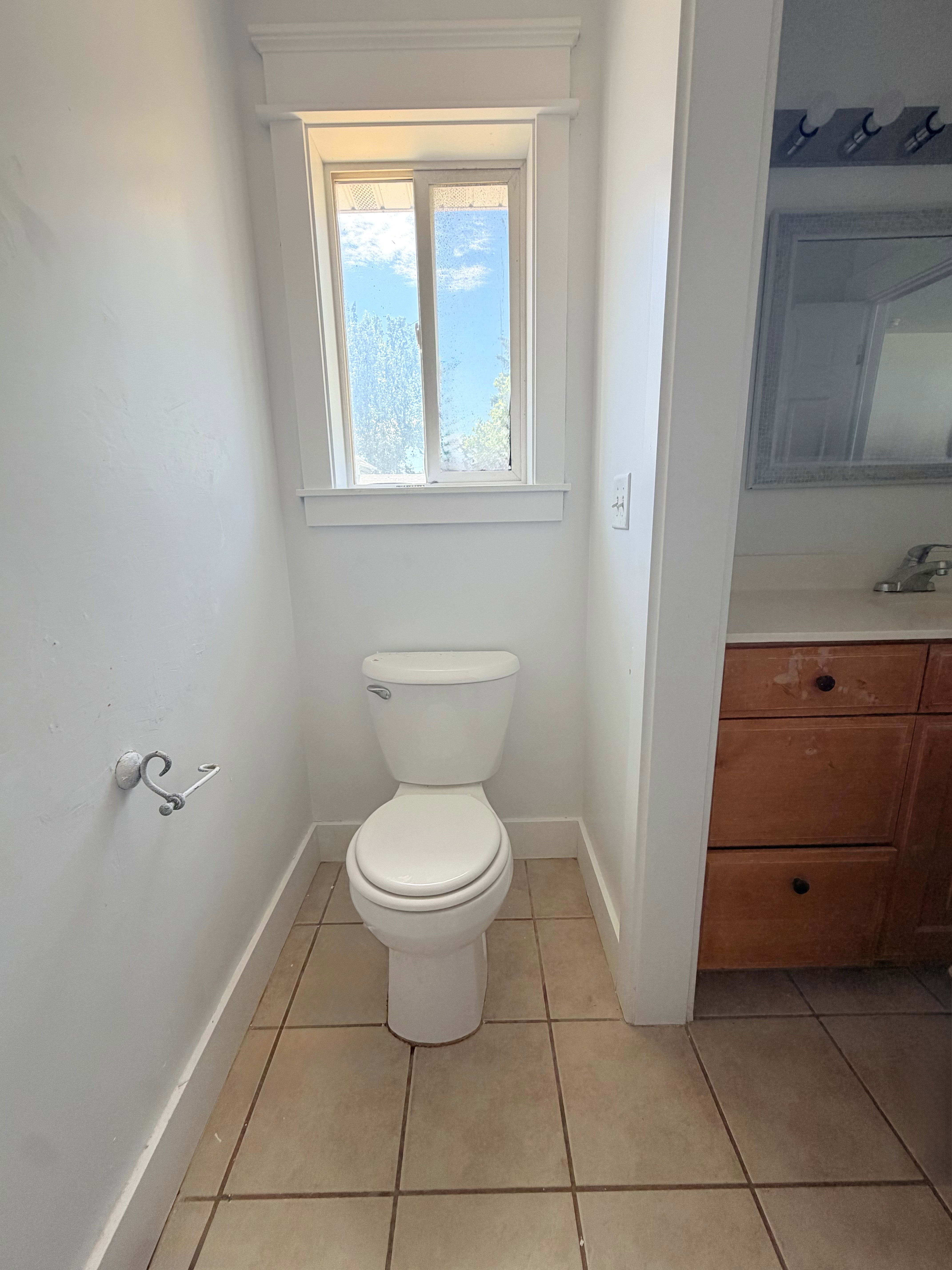 Compact half-bath featuring a white toilet, tile flooring, and a single window with white trim