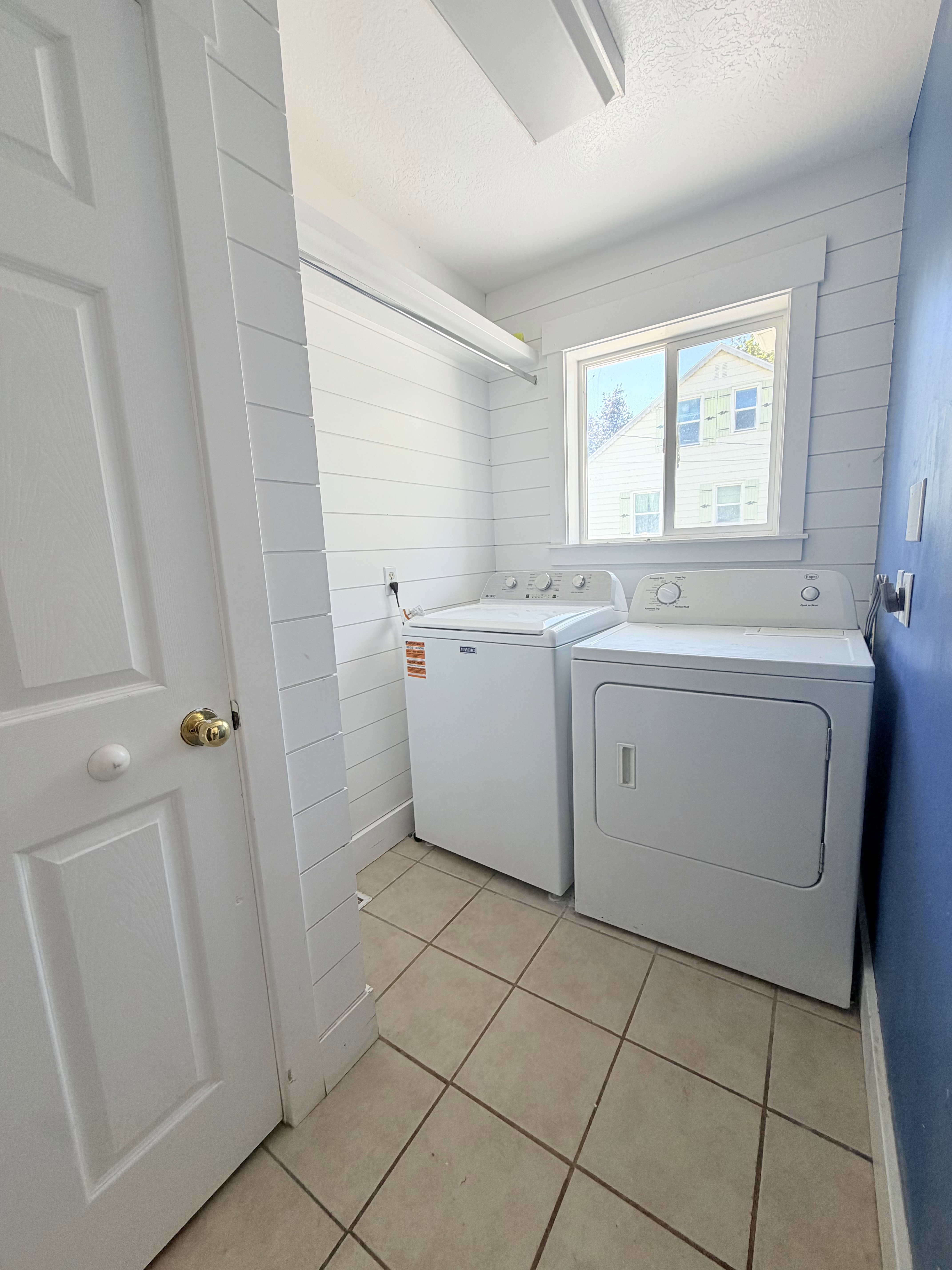 Utility room featuring ceramic tile flooring, a window, and shiplap wall treatment