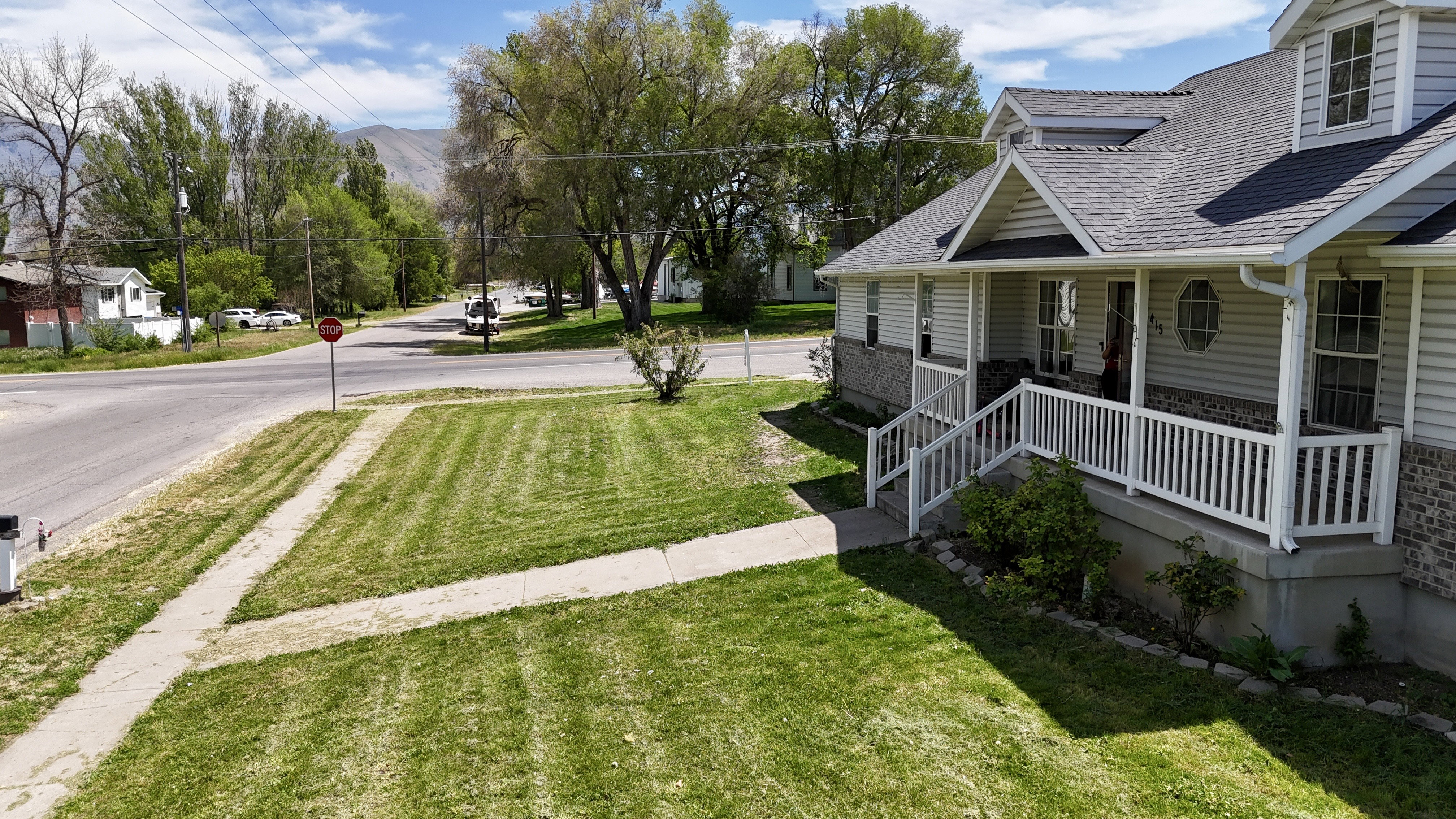 Single-family residence featuring a prominent covered porch with white railings, a light gray siding exterior, and a dark shingle roof