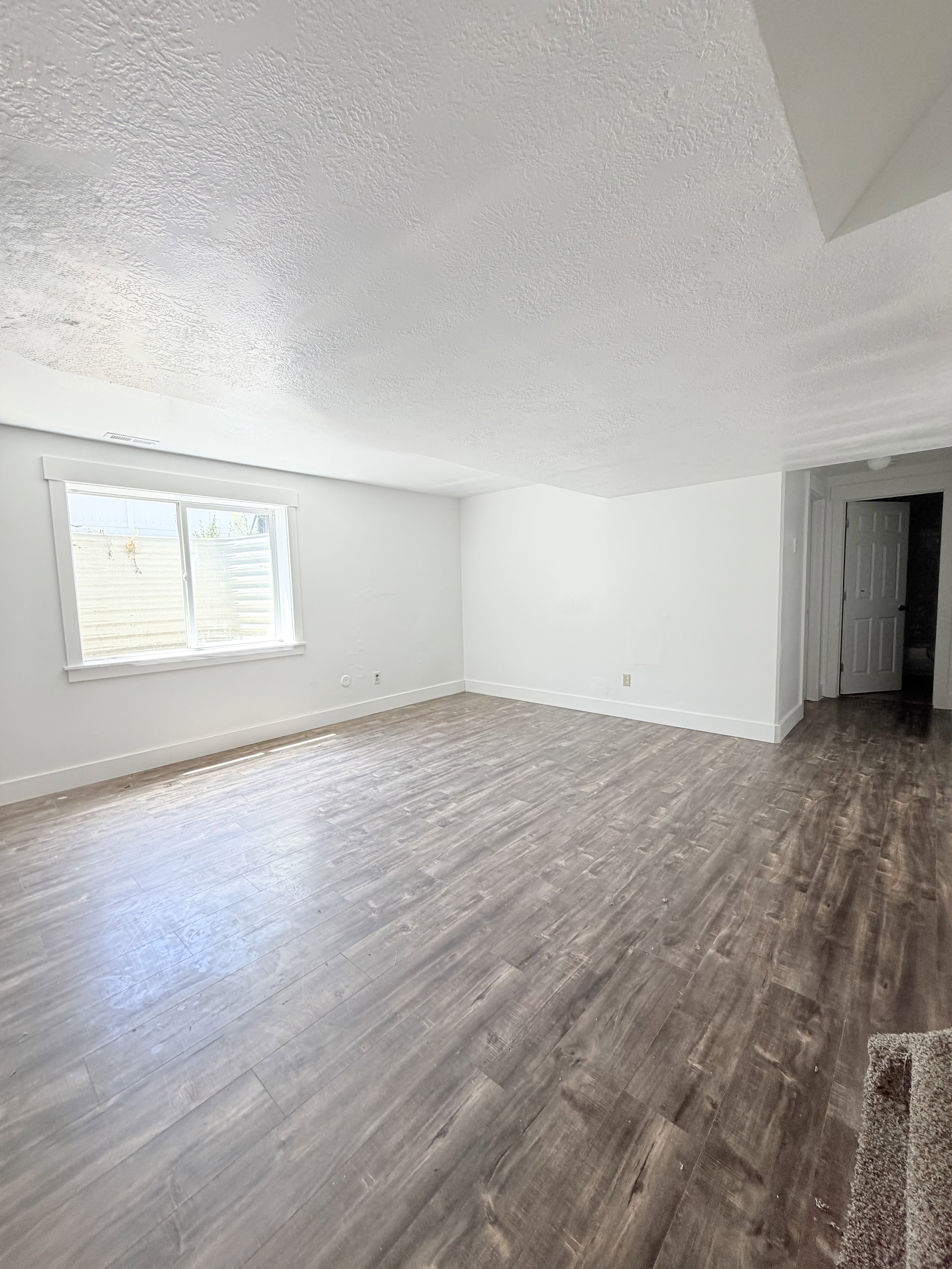 Spacious room featuring wood-finish flooring, white baseboards, and a window with a window well