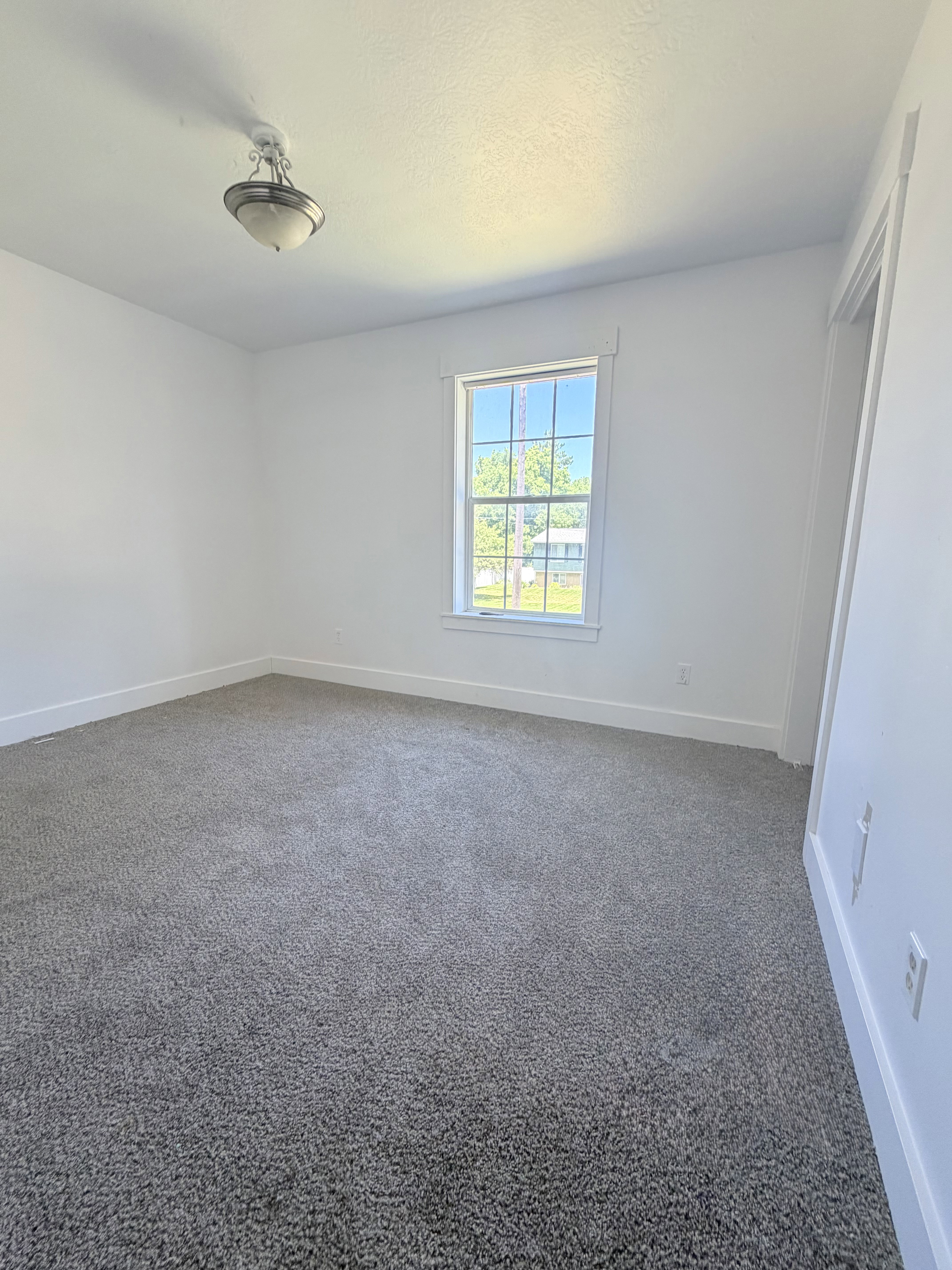 Bright room featuring a window with white trim, gray carpet flooring, white walls, and a ceiling-mounted light fixture
