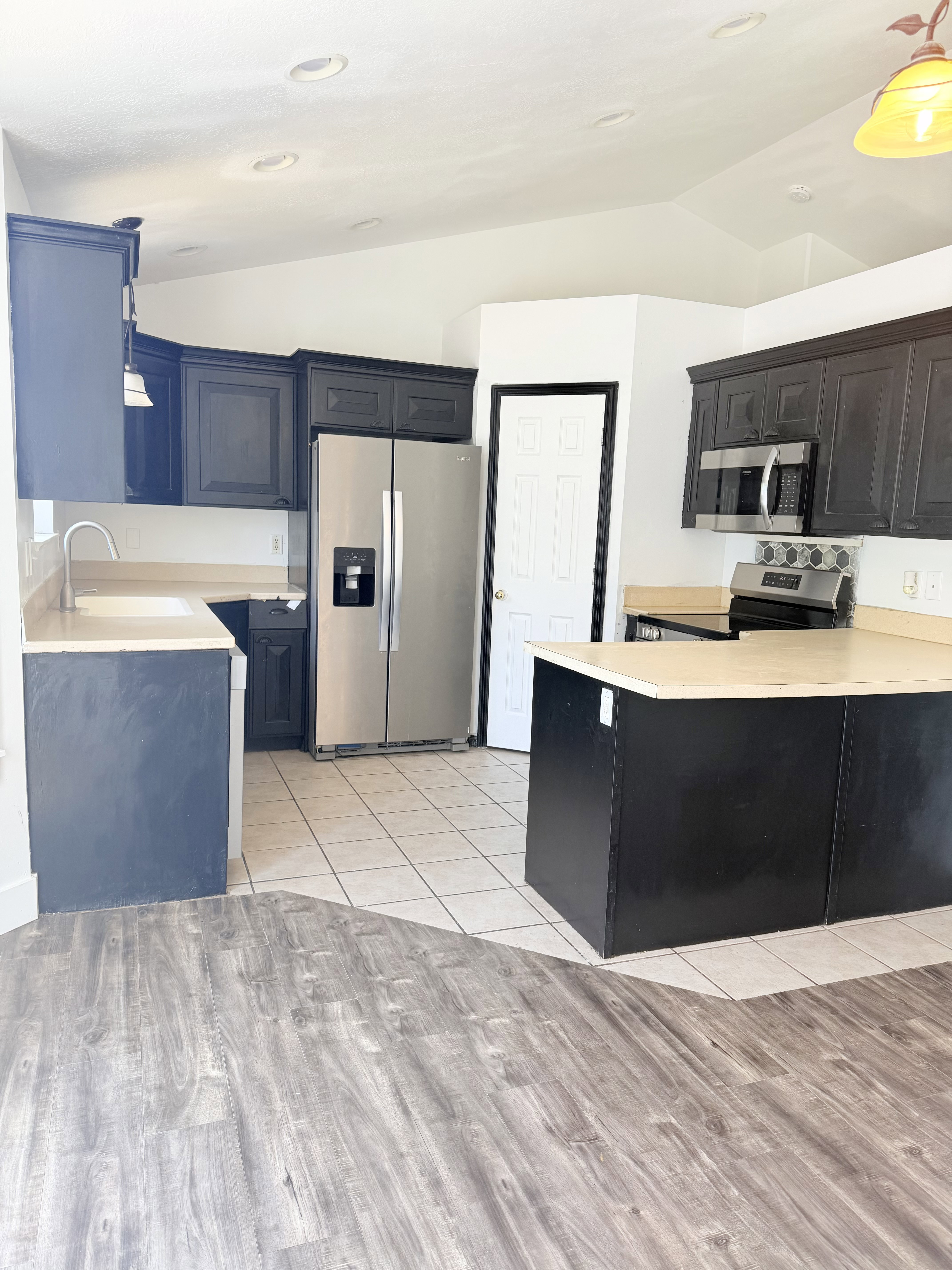 Kitchen featuring dark cabinetry, light-toned countertops, and stainless steel appliances including a refrigerator and built-in microwave