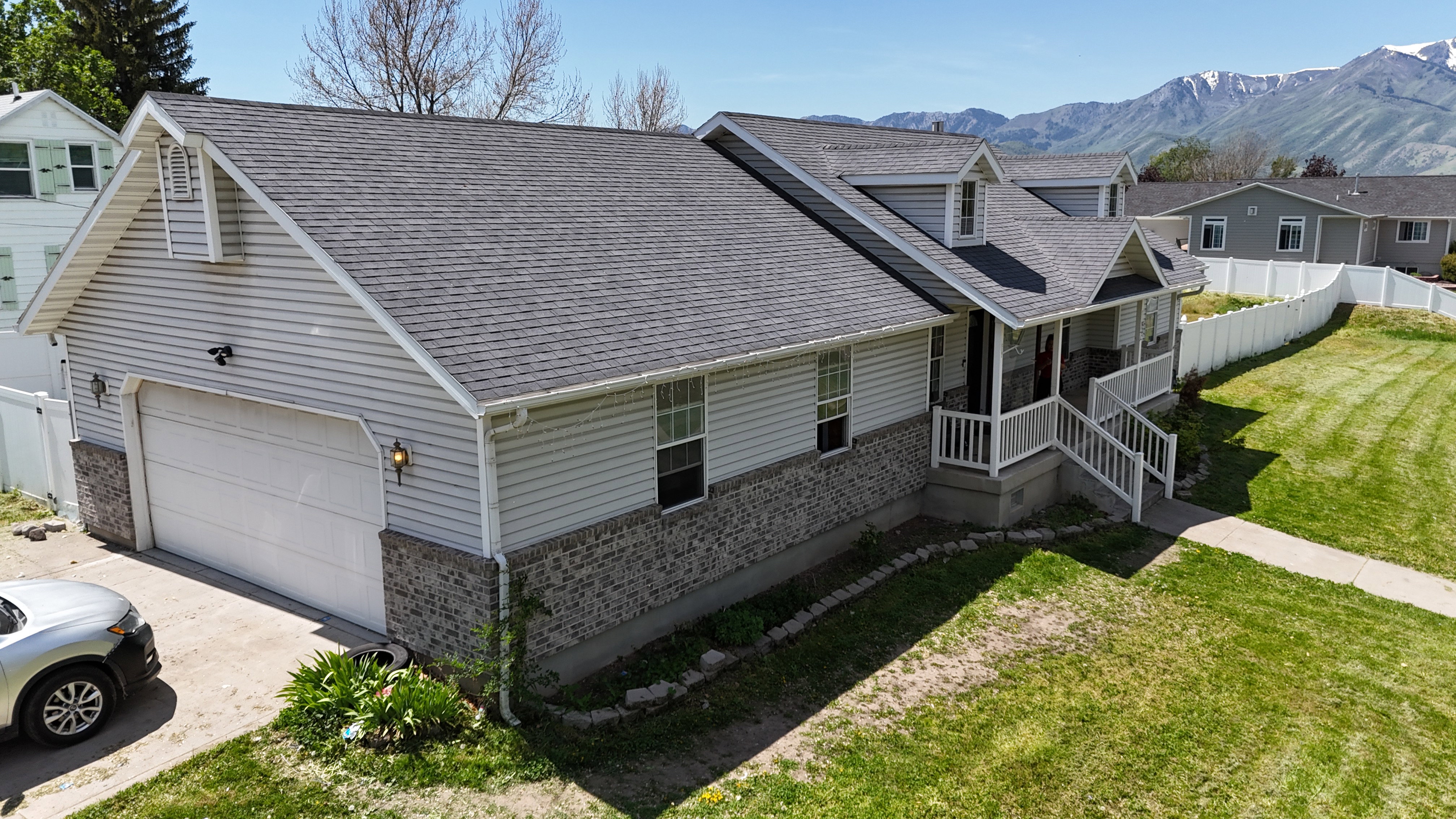 Single-story residence featuring light gray siding with a stone-finish foundation, a covered porch with white railing, and an attached two-car garage