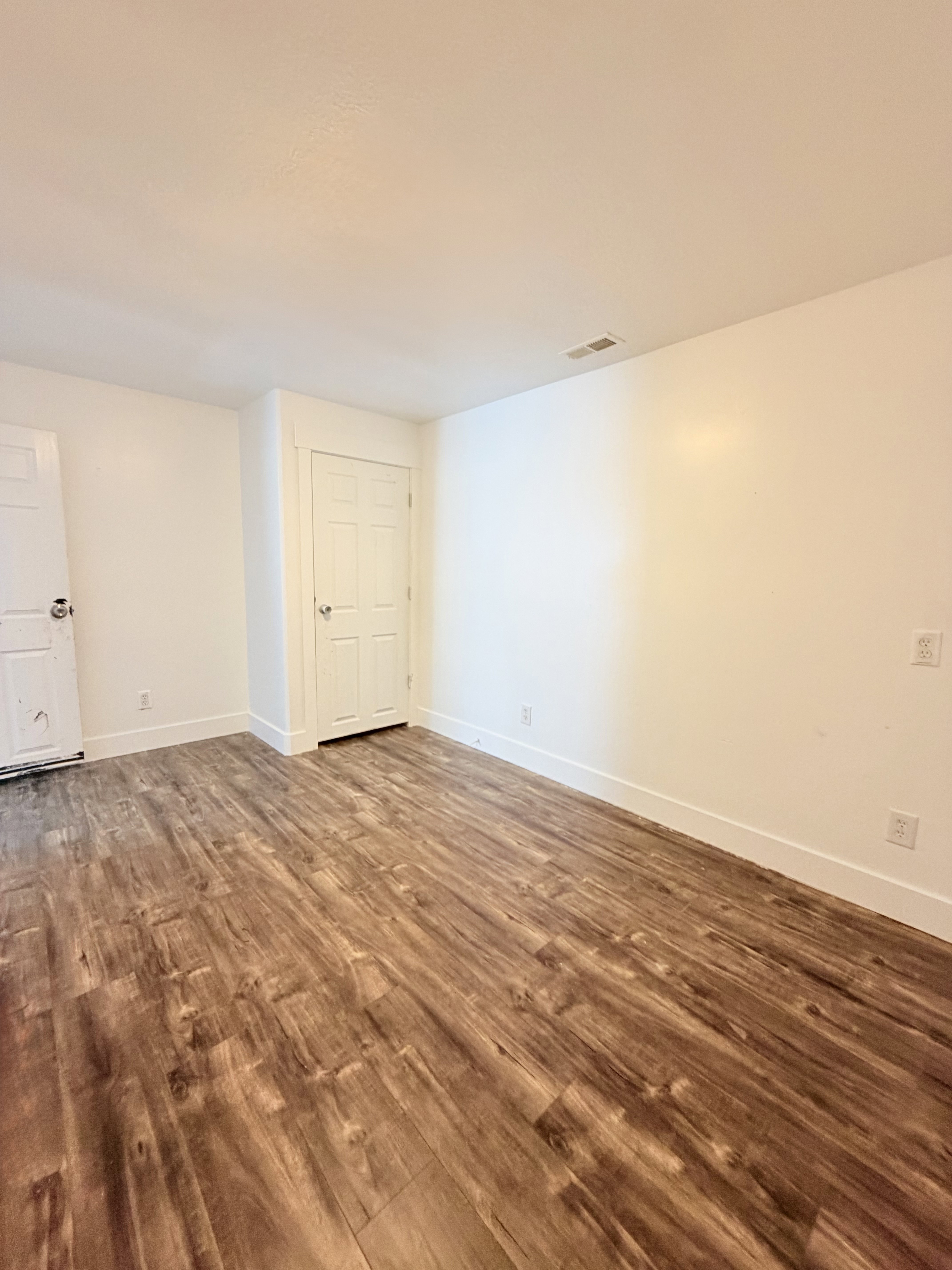 Spacious room featuring wood-finish flooring, white walls, and white trim