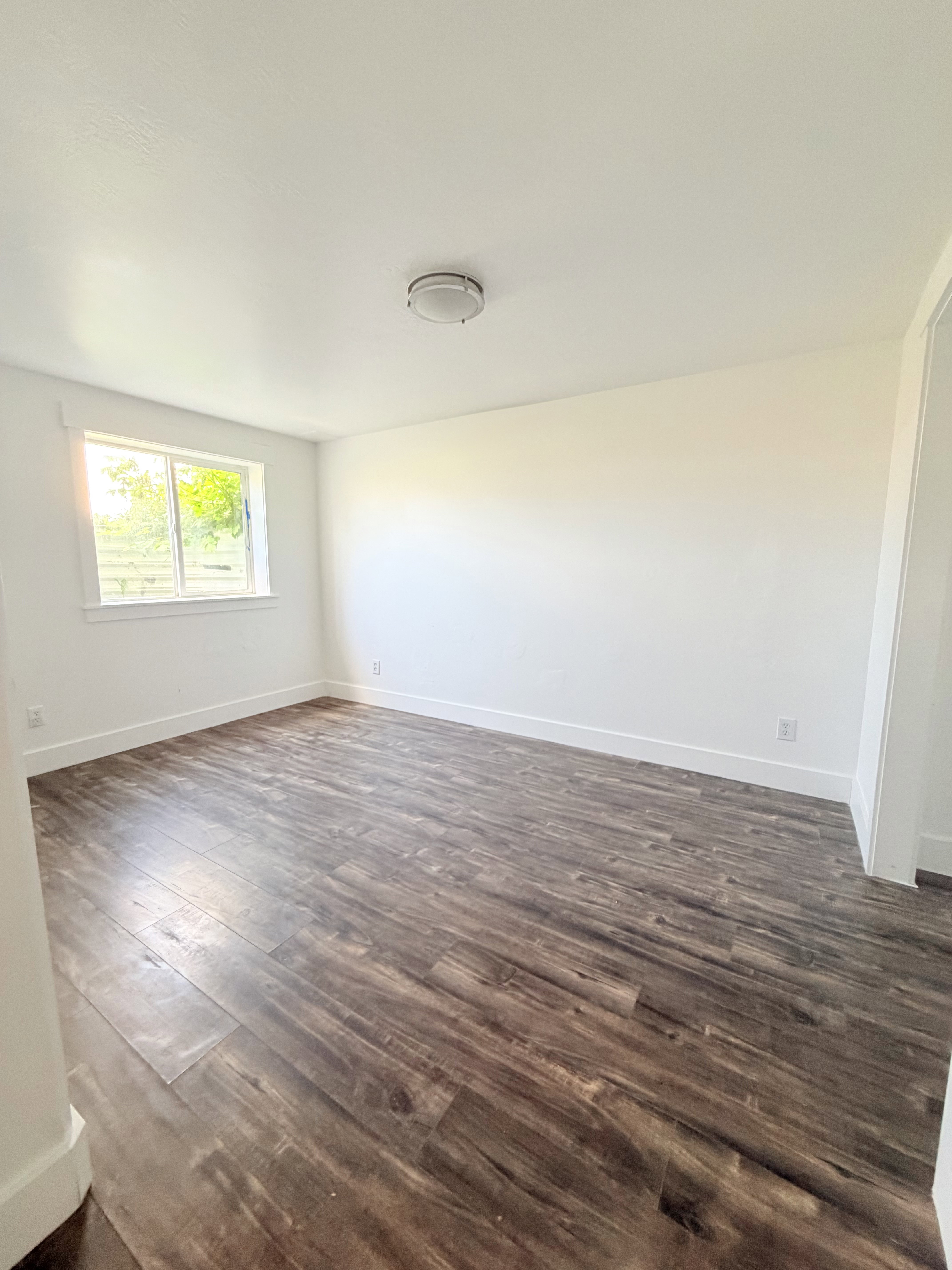 Spacious interior room featuring wood-finish flooring, white baseboards, and a neutral wall palette
